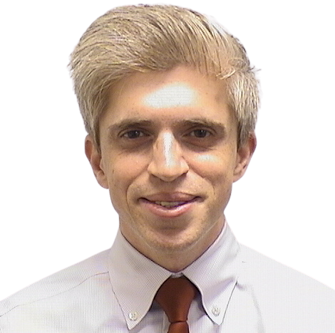 Portrait Of Mature Male Doctor Wearing White Coat Standing In Hospital Corridor