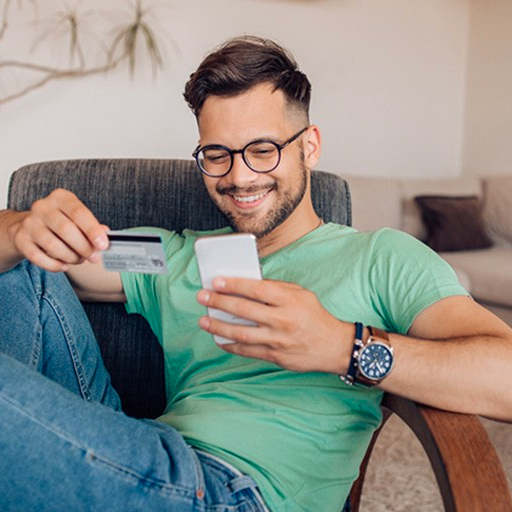 man with green shirt looking at phone and holding credit card