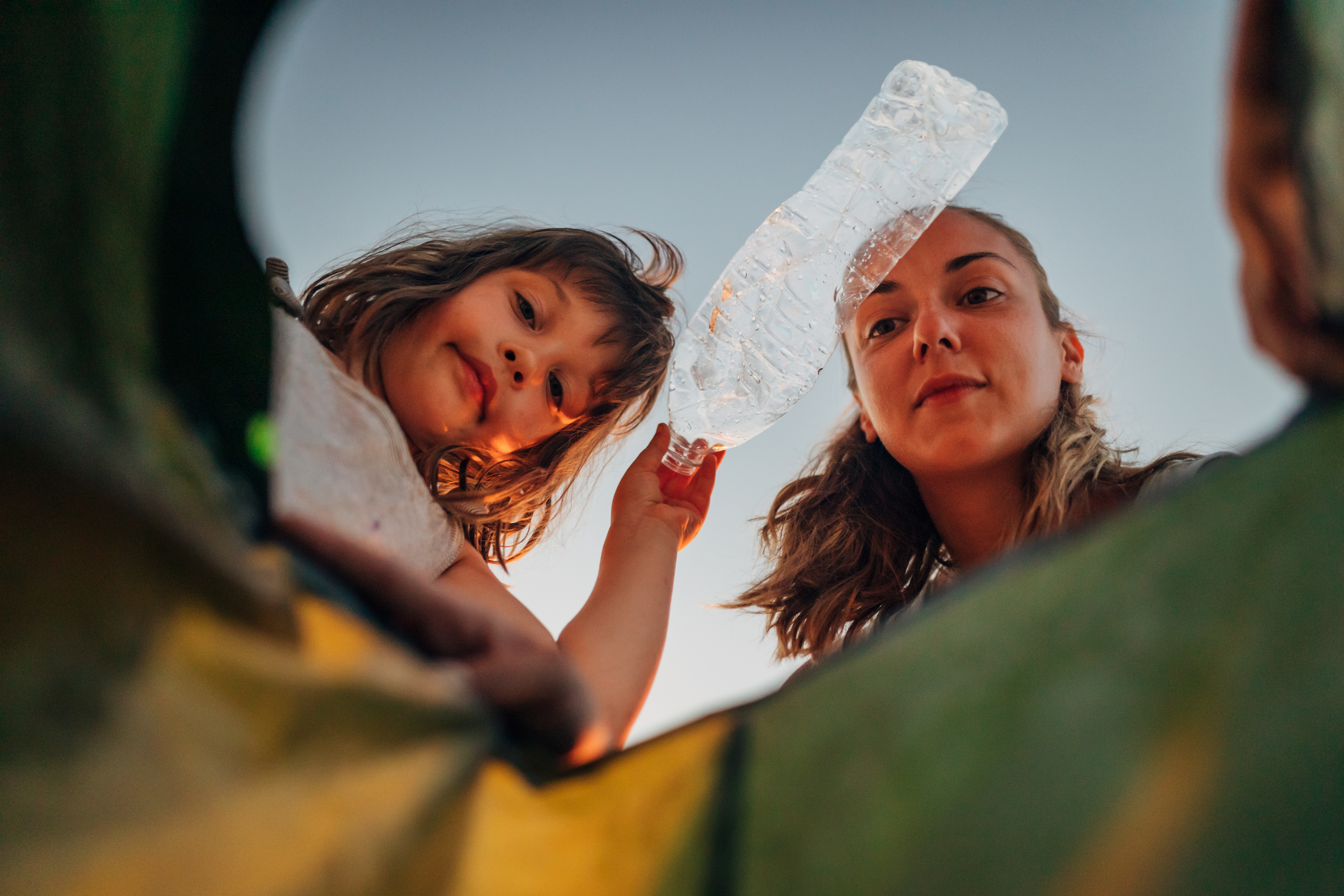 Mother and daughter putting a plastic bottle into a recycling bin