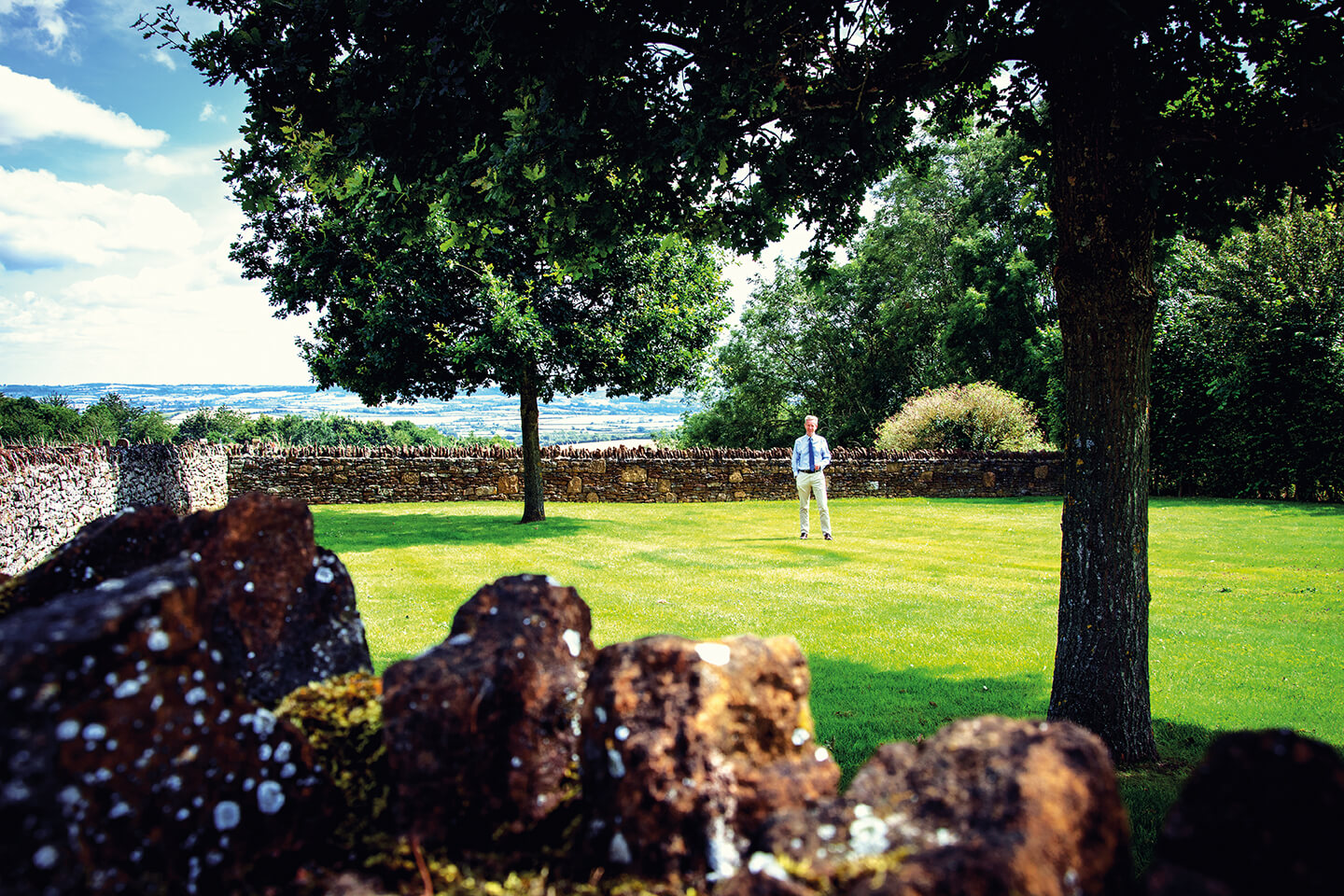 A man in a field in front of a view of the Cotswolds