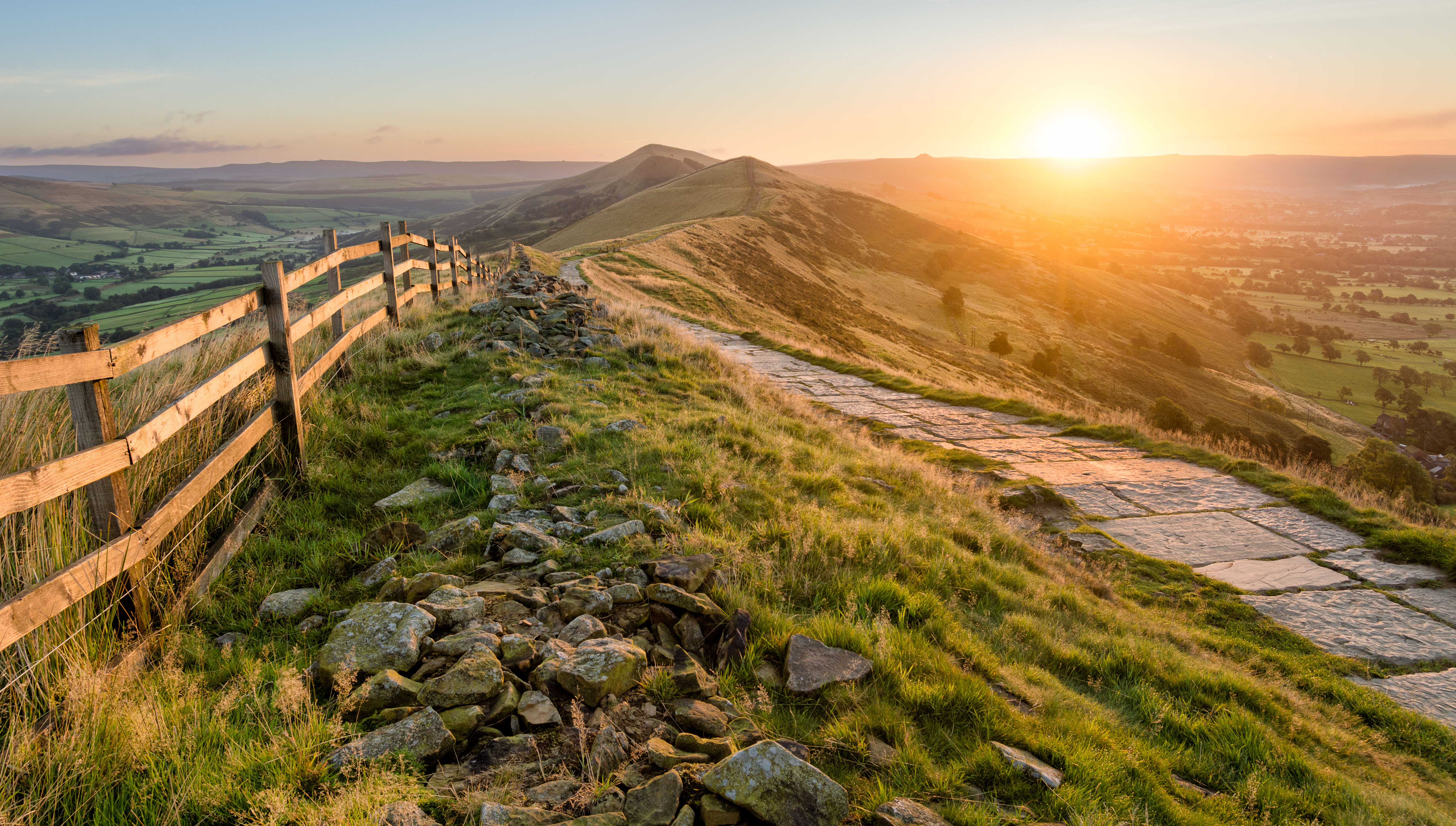 A stone footpath and wooden fence leading a long The Great Ridge in the English Peak District. Taken at sunrise, the image features beautiful Autumn vibrant colours from the rising sun.