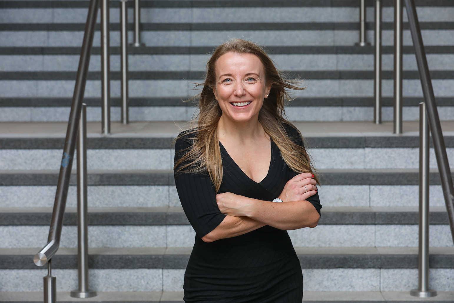 A picture of Becky Ellis, BTR Operations Manager stood smiling with arms crossed in front of a flight of stairs with steel railings