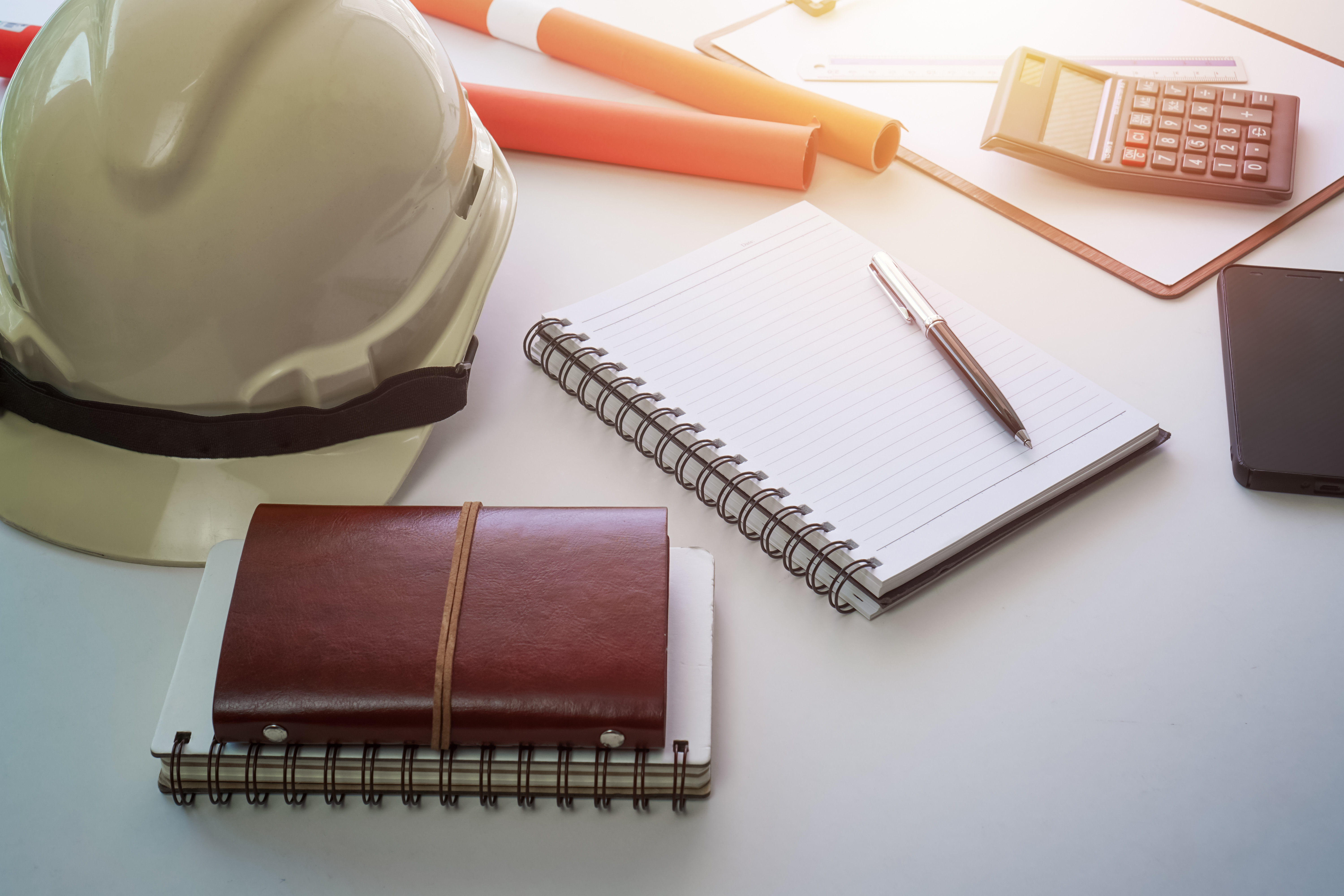 Hard safety hat and notepad on working desk. Project management concept.