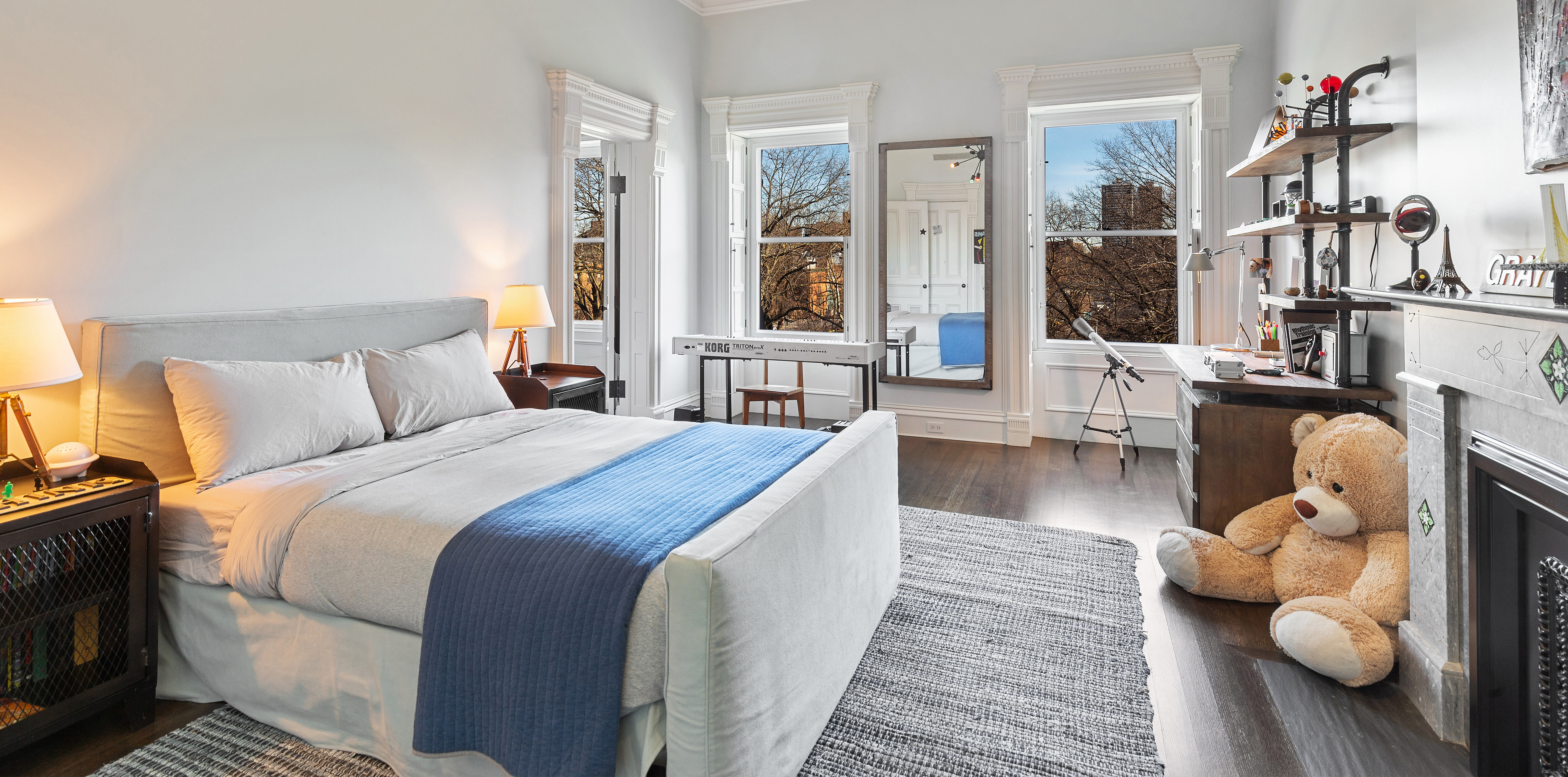 A bedroom with dark wood floors and a decorative fireplace, decorated with a Korg keyboard, and a telescope.
