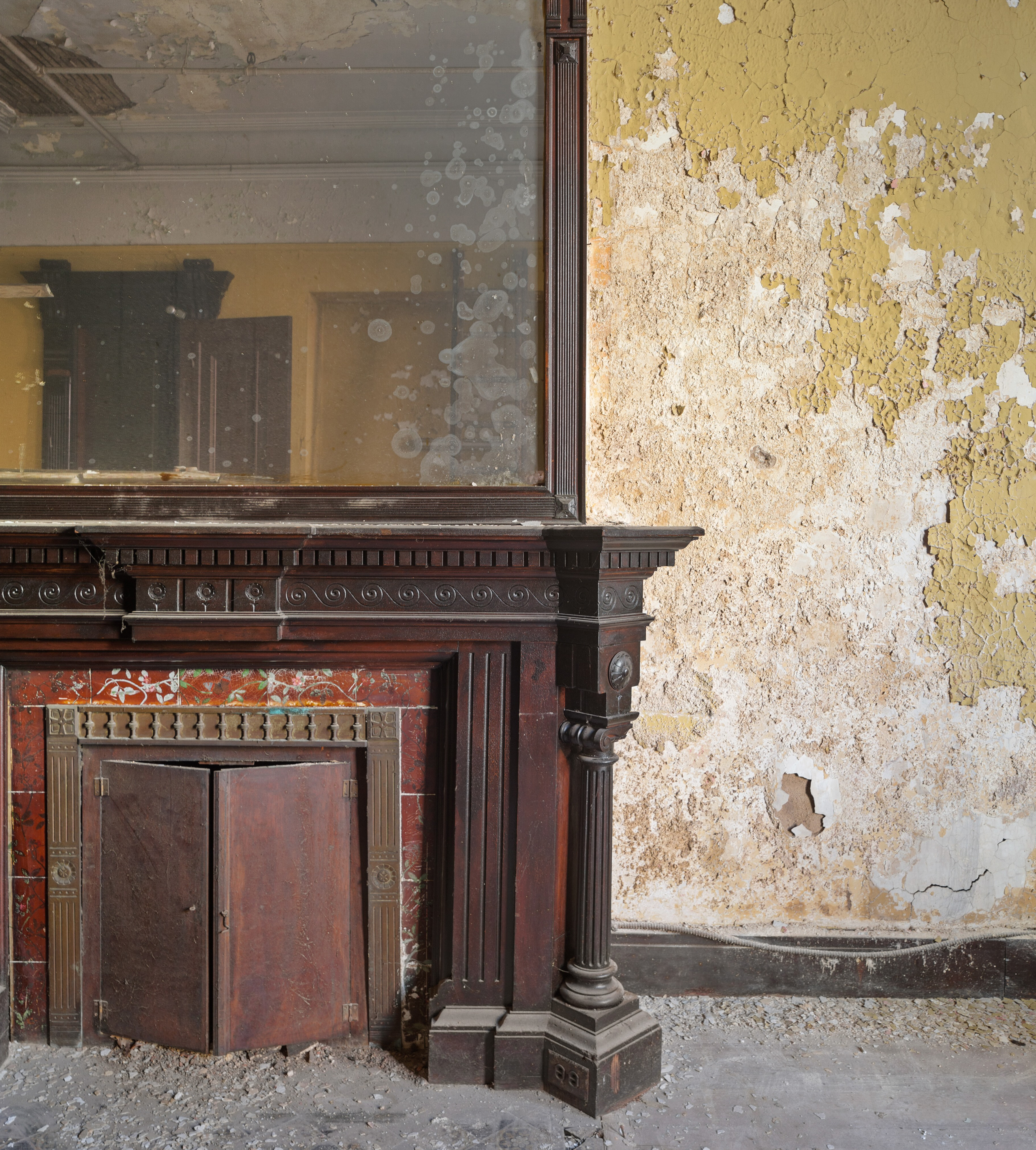 An ornate wooden fireplace, topped by a large mirror, showcasing period details and old-world craftsmanship, with intricate carvings and decorative tiles.