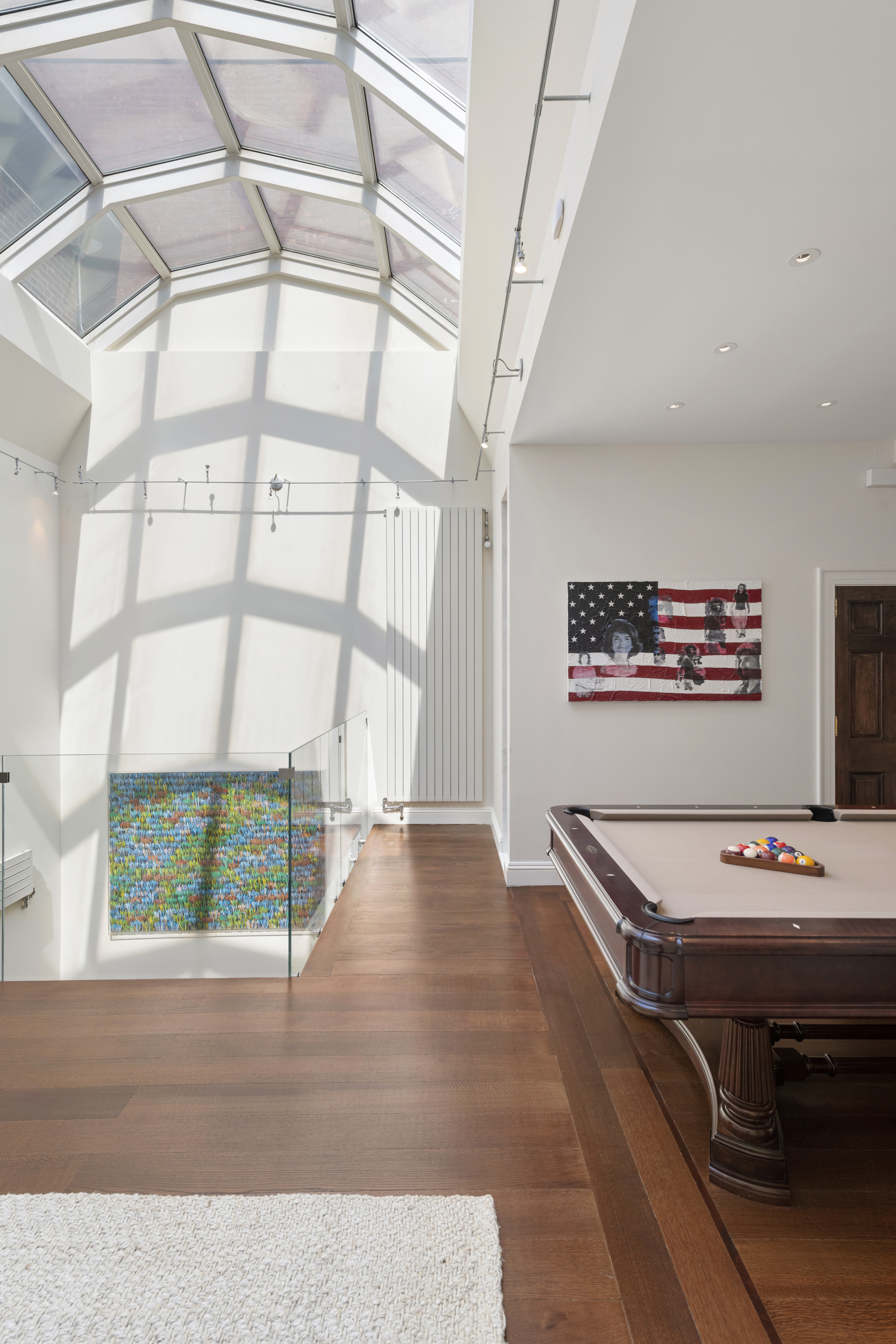 Modern room with a skylight ceiling, wooden floors, a pool table with balls arranged for play, and an American flag-themed artwork on the wall.