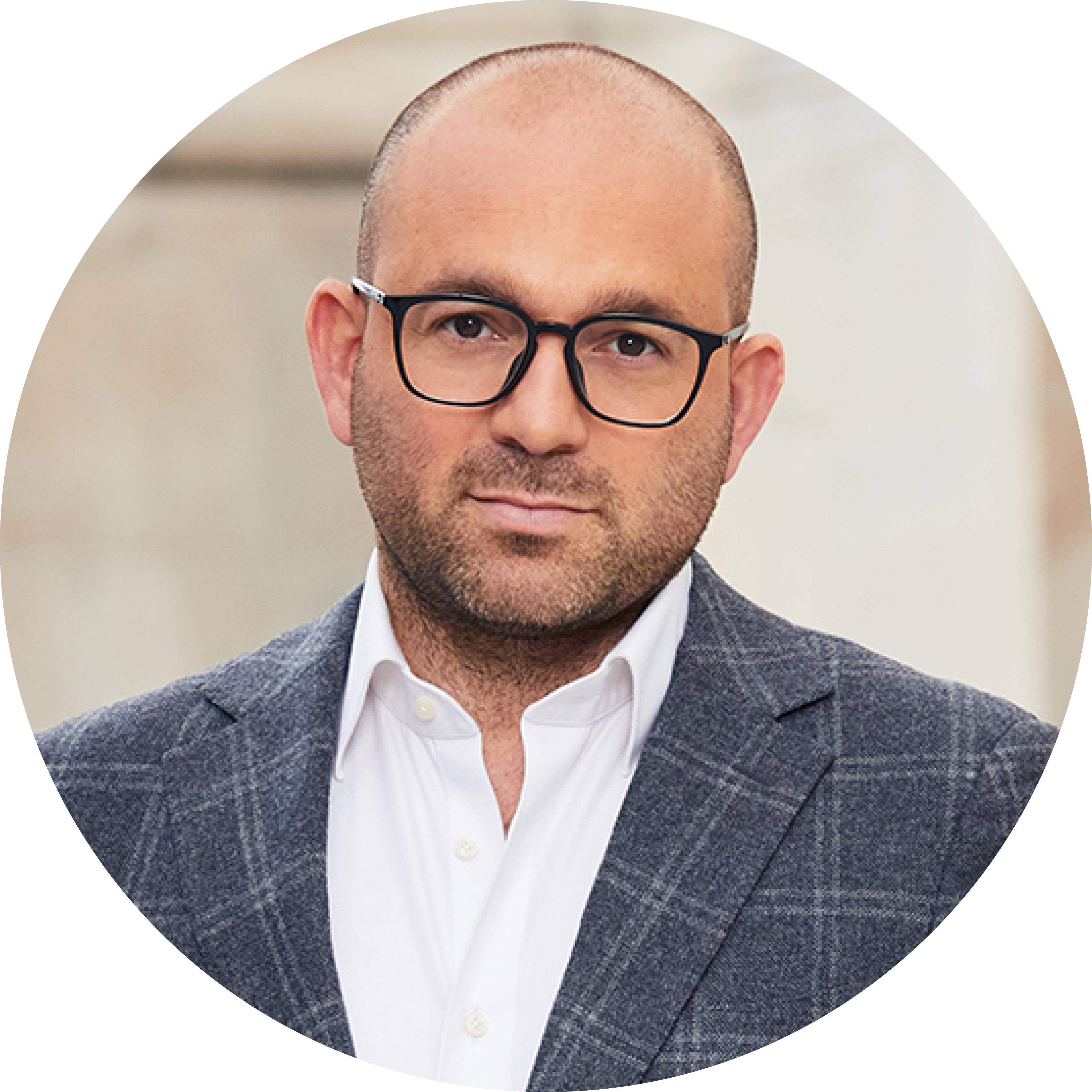Person wearing a white shirt and dark checkered blazer, standing against a neutral background.