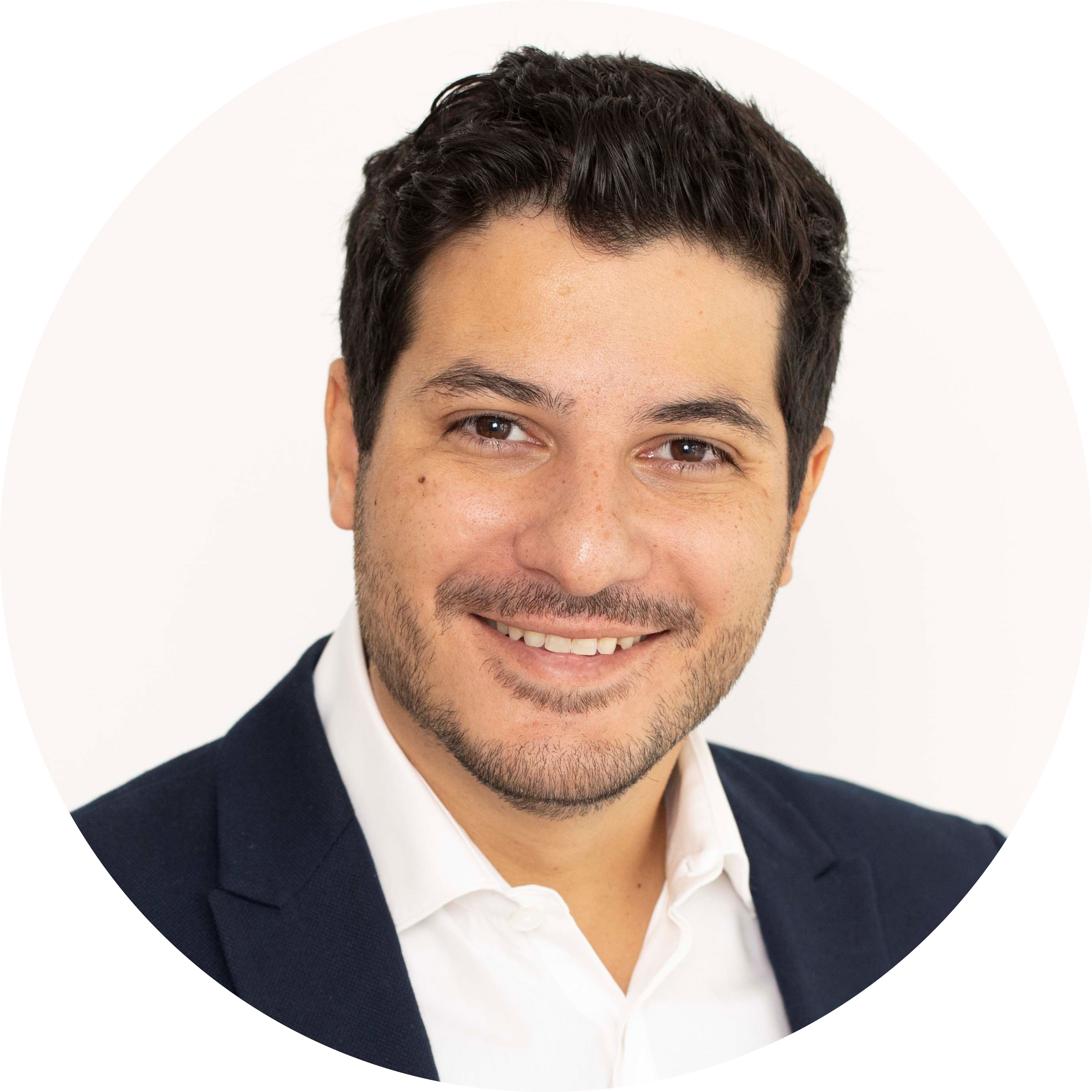 Person wearing a dark suit jacket and white dress shirt standing against a plain white background.