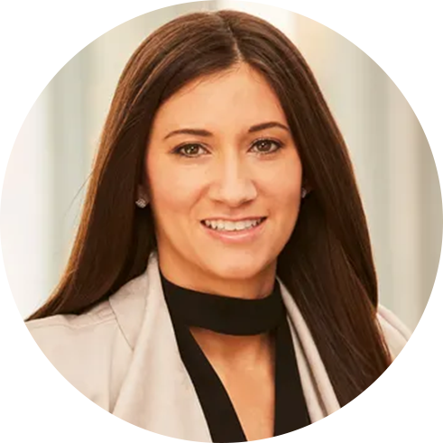 A person with long, straight hair wearing a light-colored blazer and a black top with a high neckline.