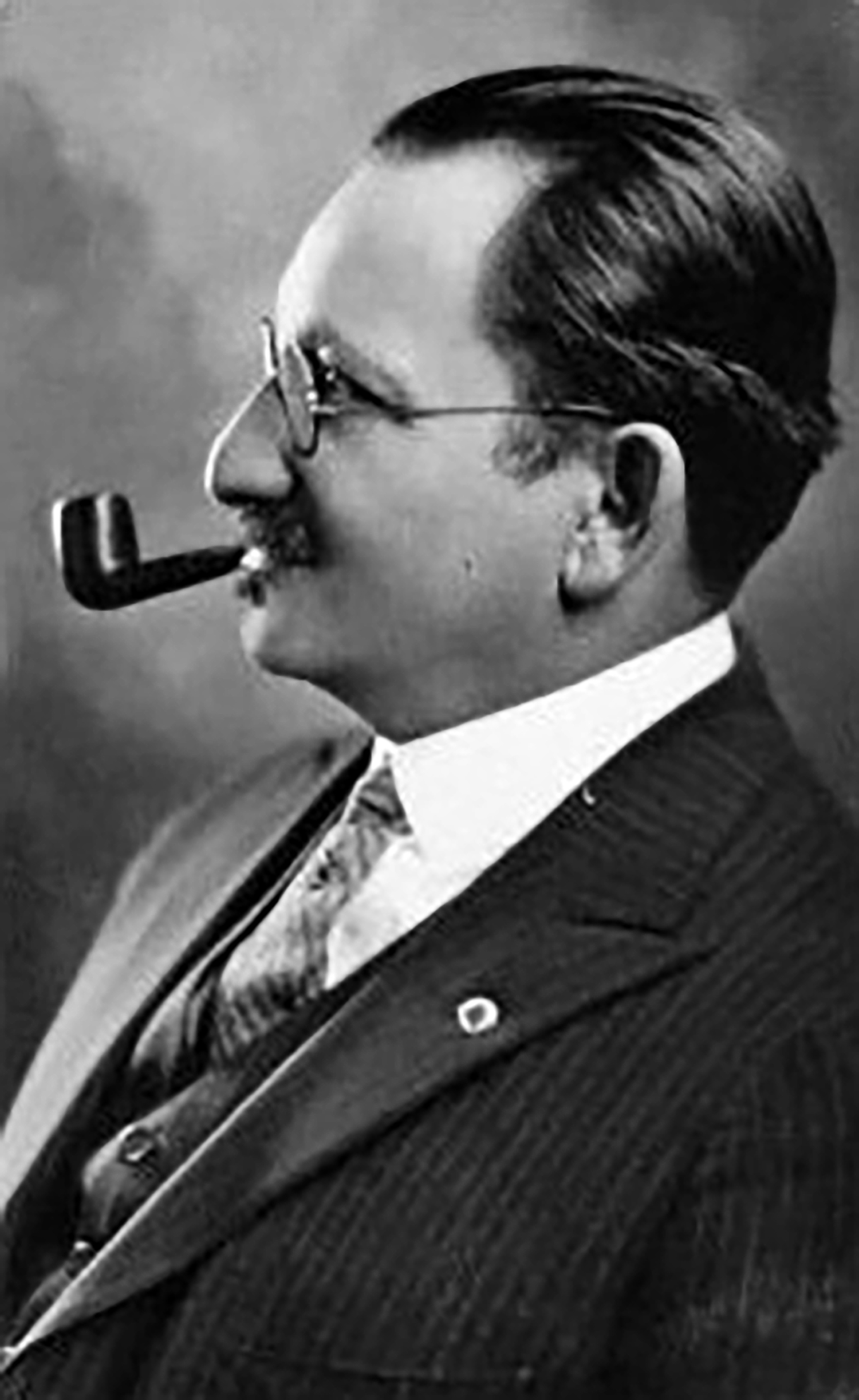Black and white photo of Emery Roth wearing a suit with slicked-back hair and smoking a pipe.