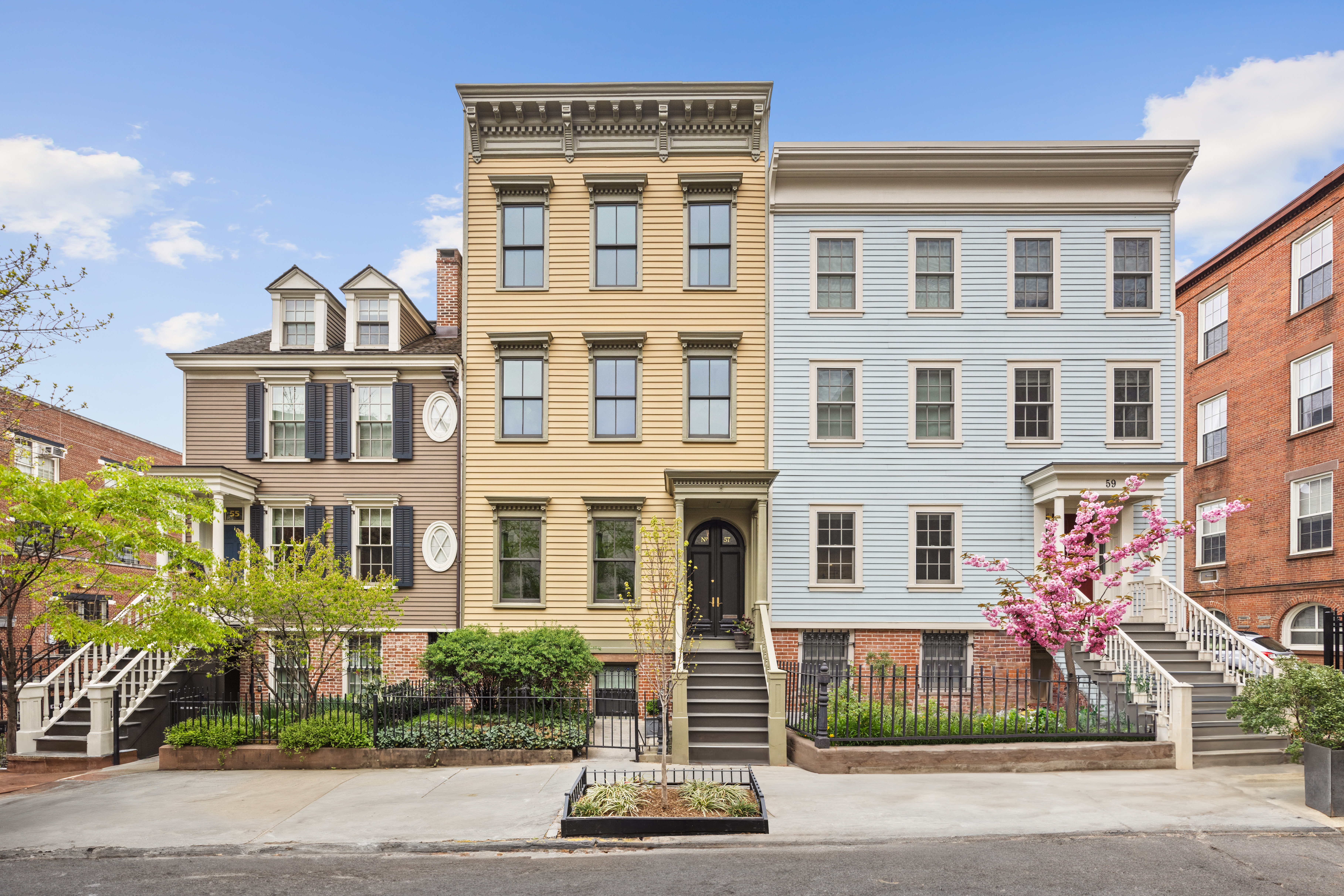 Three adjacent townhouses with unique architectural styles and colors, each with steps leading to the entrance, small front gardens, and a clear blue sky in the background.