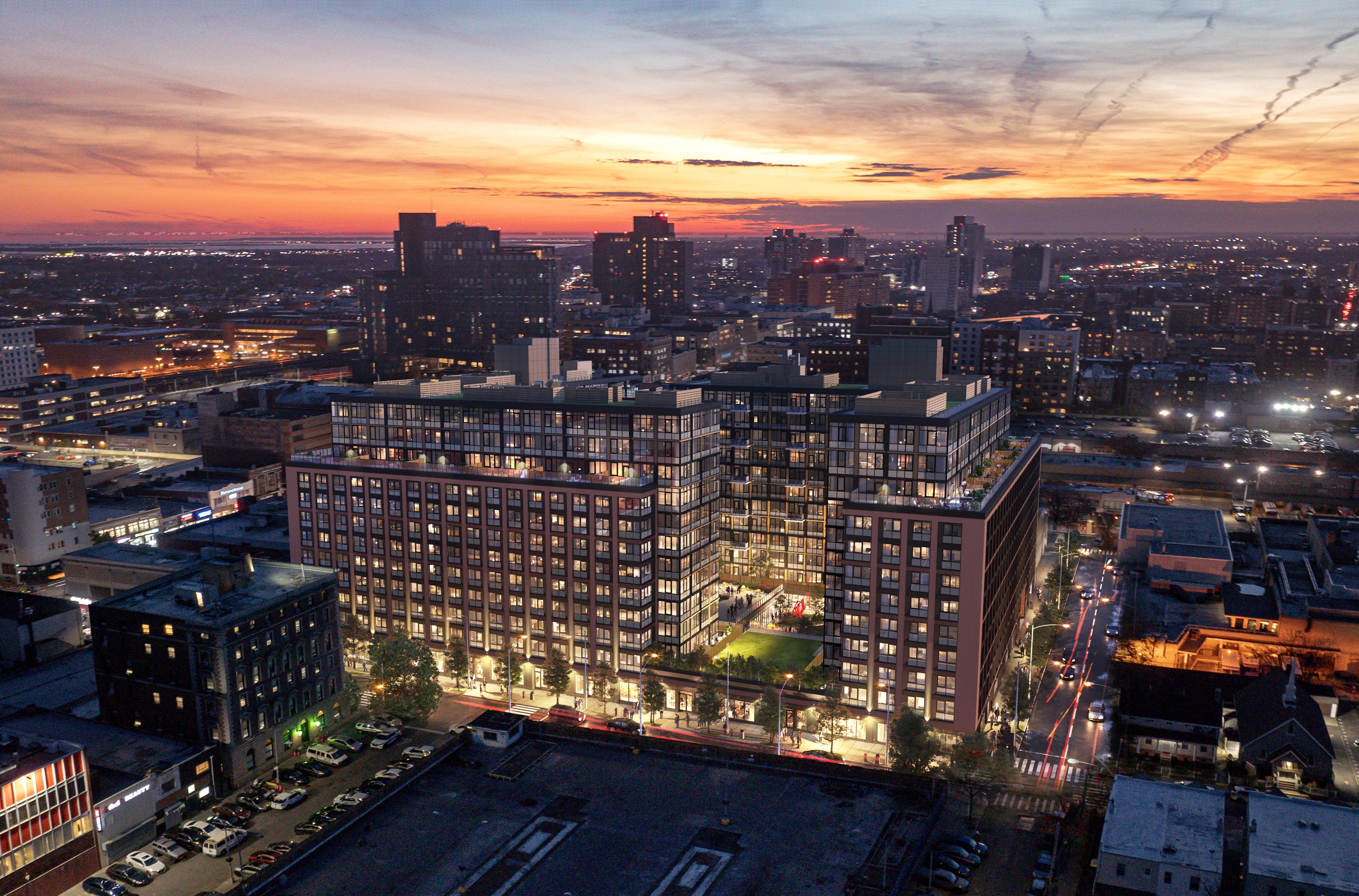 Aerial view of a cityscape at sunset with a prominent modern building complex in the foreground, surrounded by other buildings and illuminated streets.