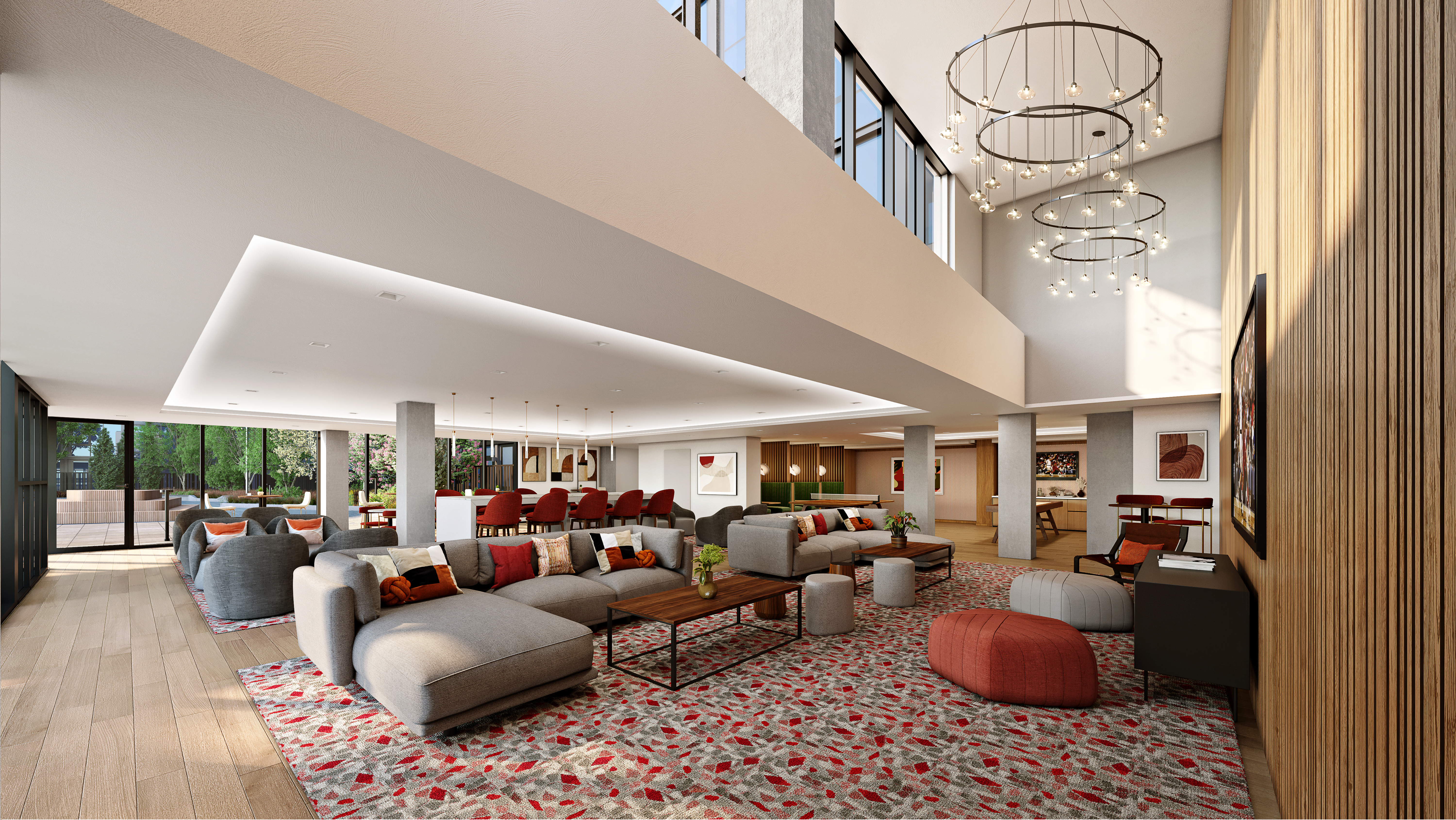 A spacious, modern lounge area with large windows, gray sofas, red ottomans, a patterned carpet, high ceilings with circular chandeliers, and abundant natural light.