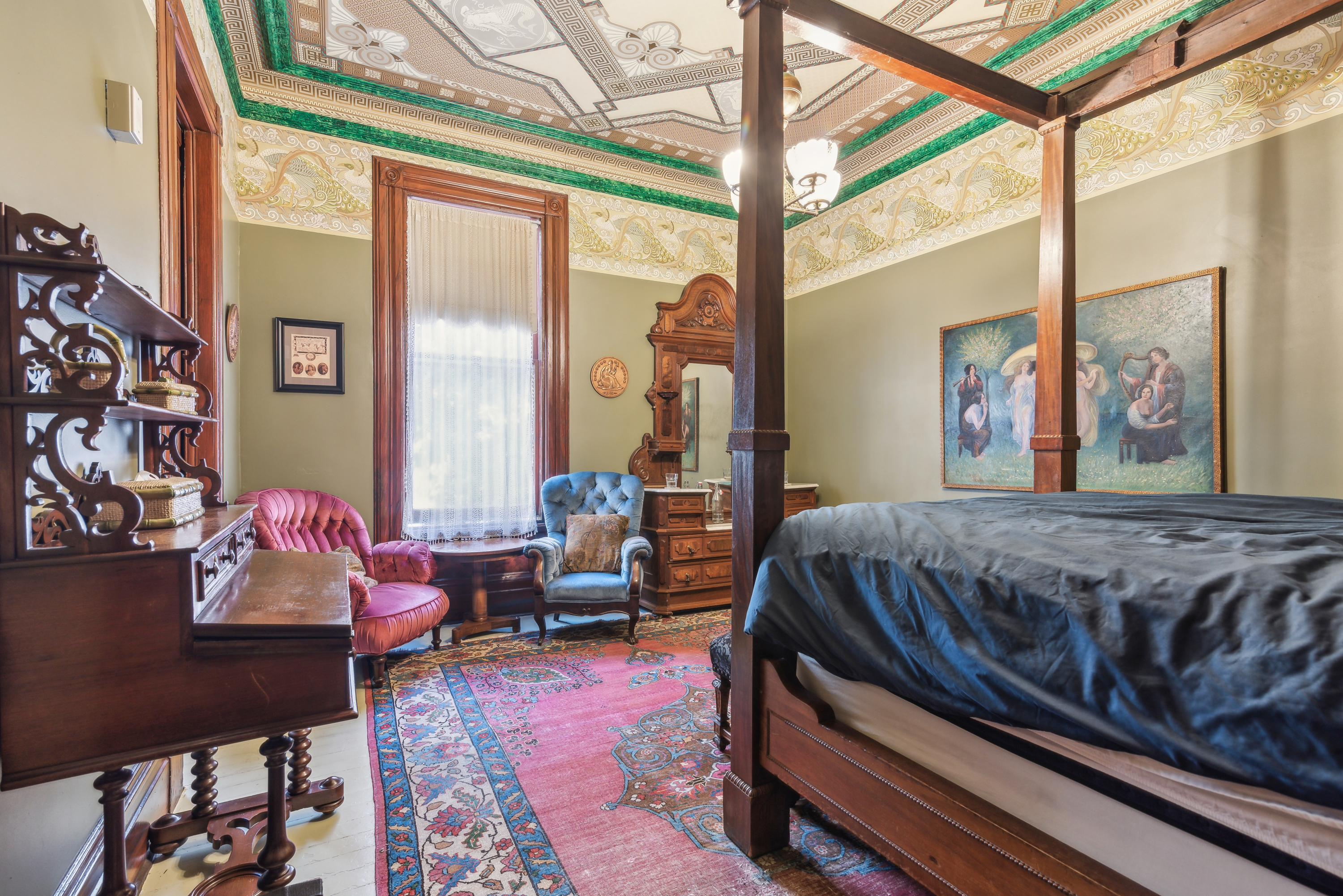 An ornate bedroom with a bed, decorated ceiling, and two tufted chairs.