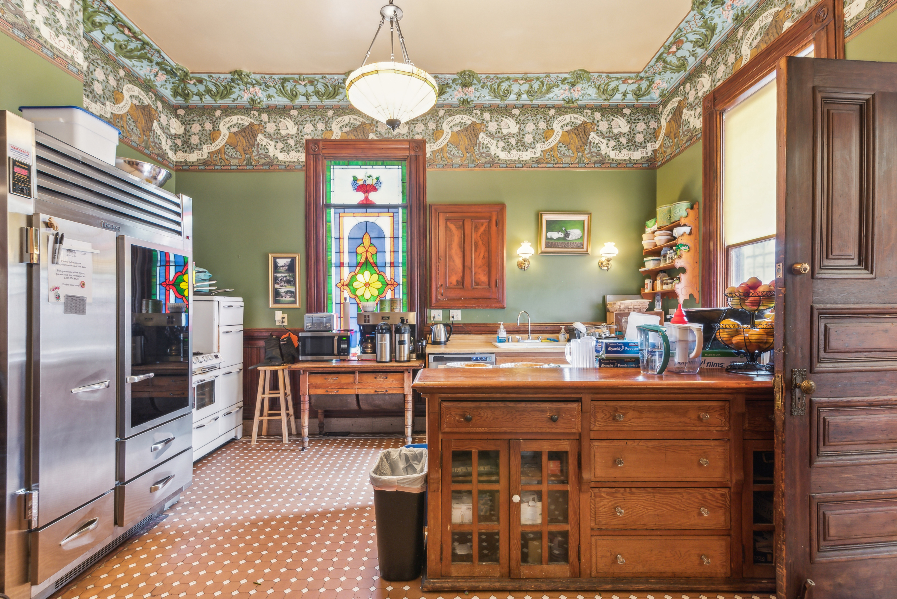An ornate, old-fashioned style kitchen with white cabinetry, stainless steel appliances, and a central island with barstools.