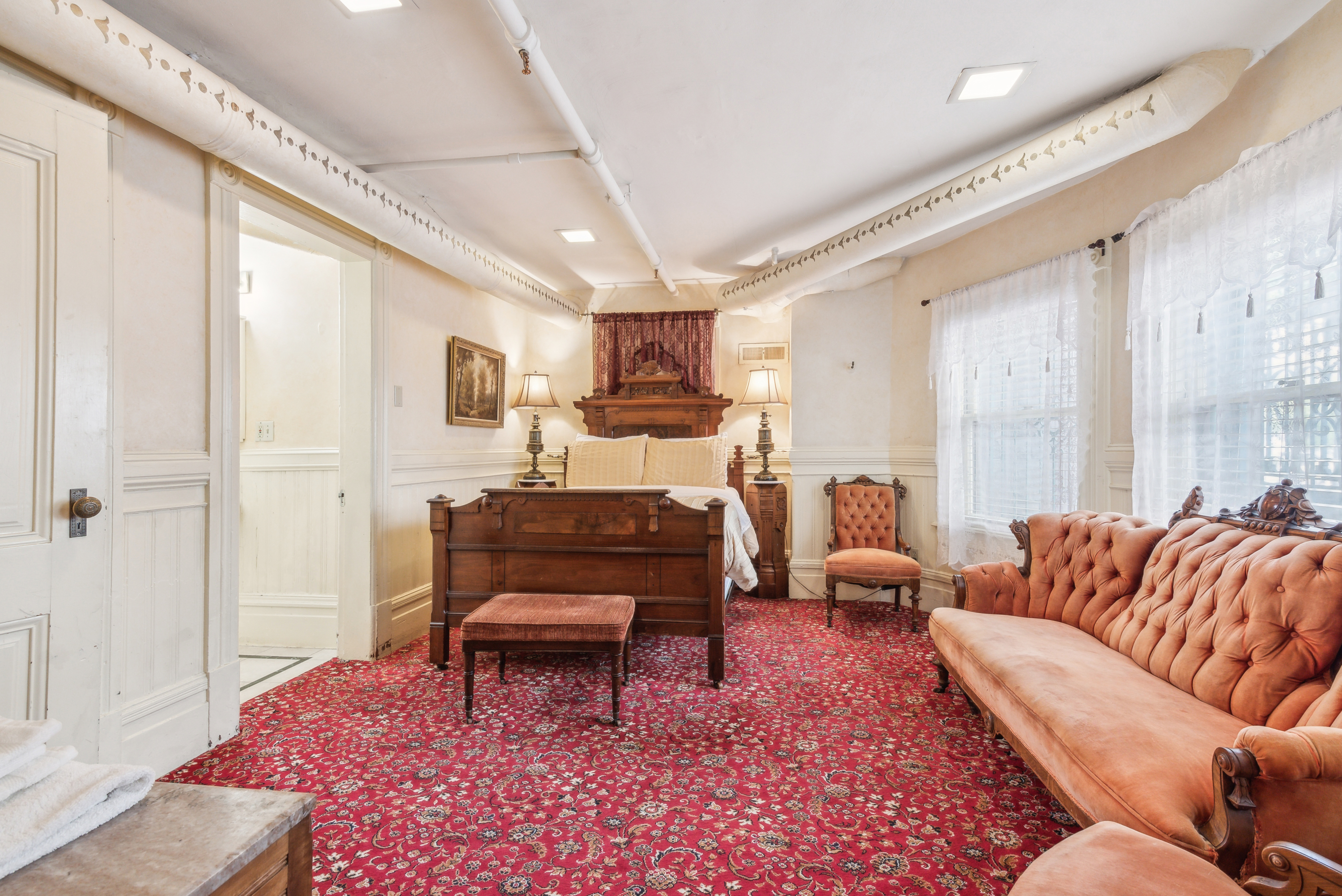 A  bedroom with windows on one side, a red patterned carpet, and a pink tufted sofa.
