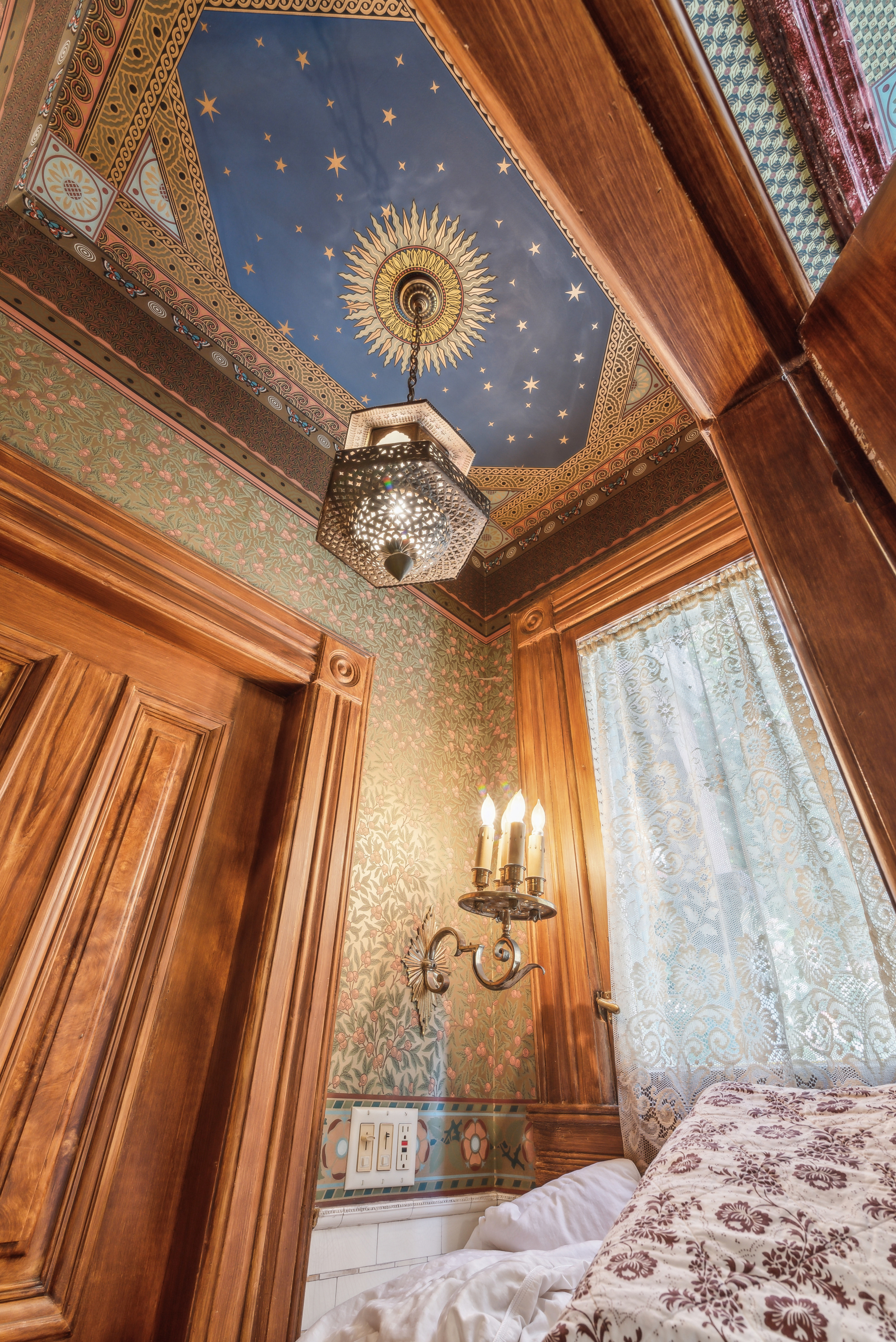 A close-up view of an ornate ceiling with a blue background adorned with golden stars and decorative molding. A chandelier hangs from the center of the ceiling.