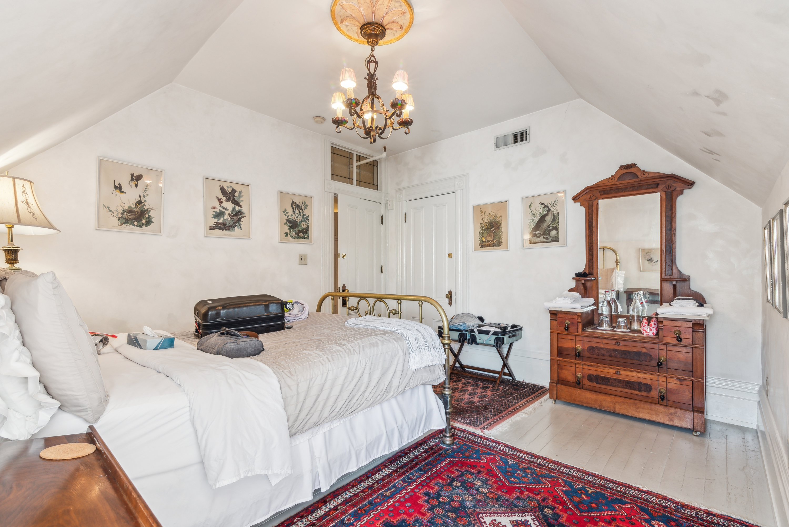 White bedroom with vaulted ceiling, red rug, and a dresser.
