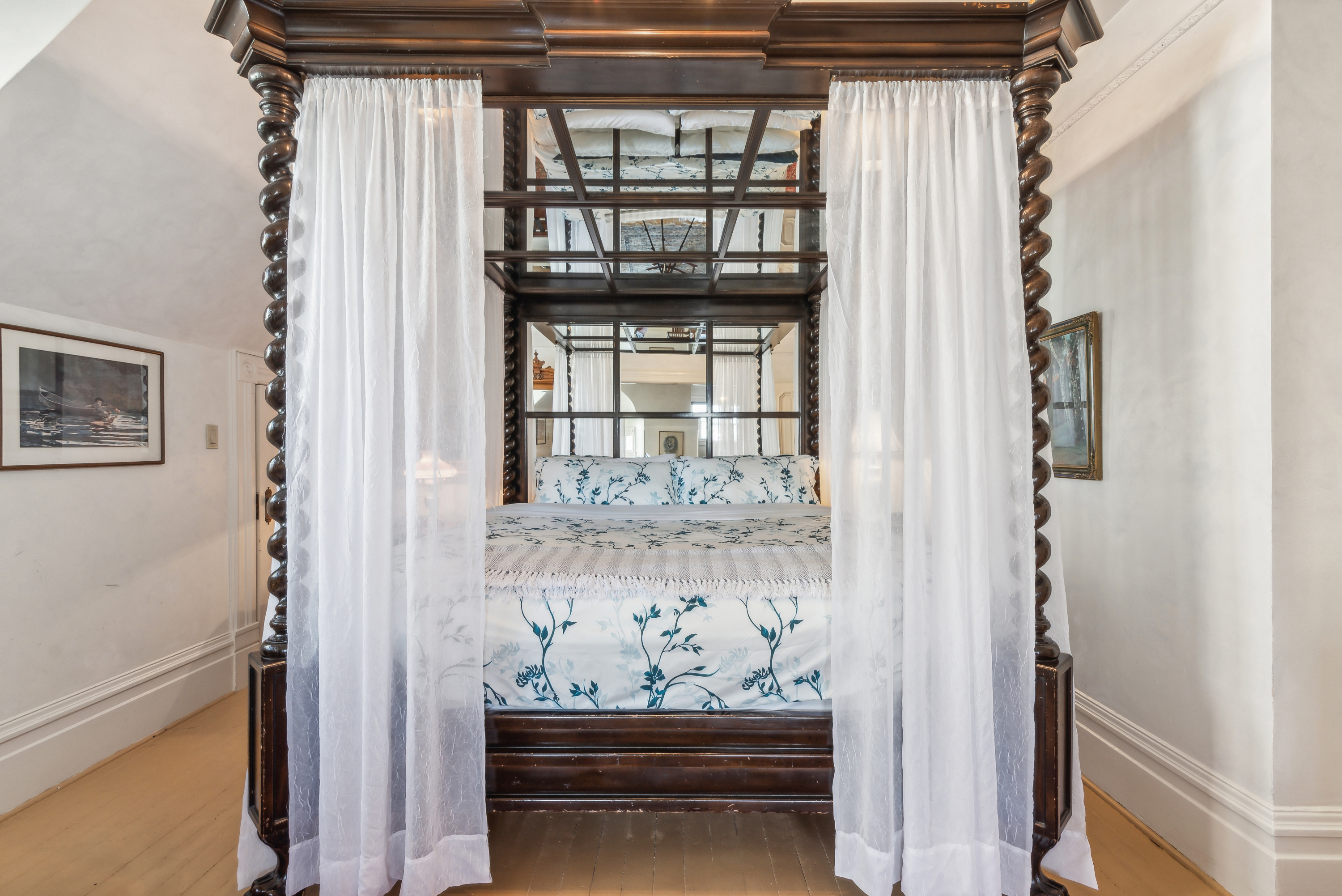 Ornate dark wood four-poster bed  in a white bedroom.