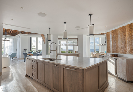 Modern kitchen with a central island, pendant lights, large windows, and a dining area in the background.