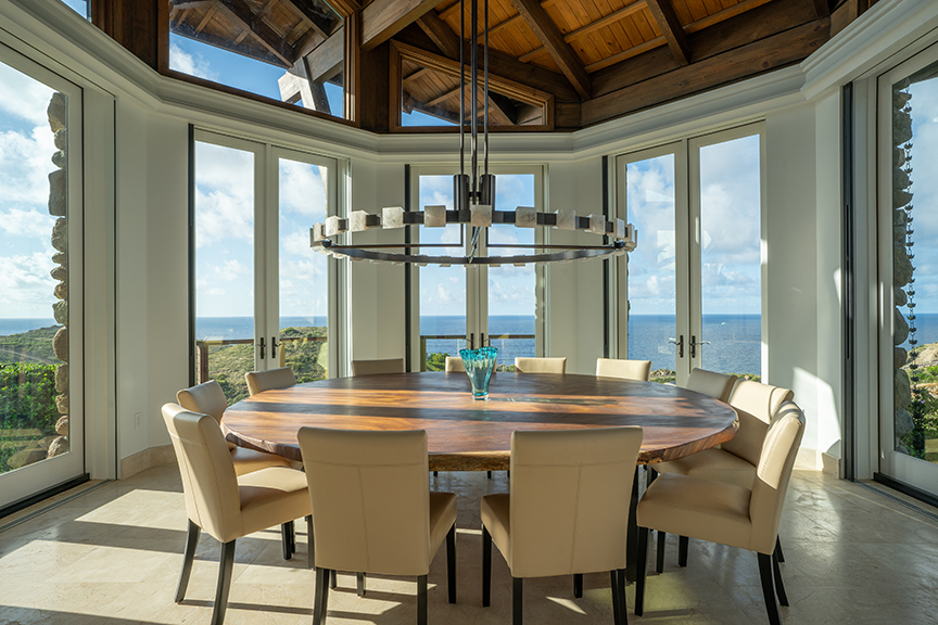 Dining room with ocean view, round table, and vaulted ceiling.