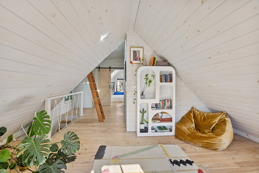 Cozy attic with bookshelf, bean bag, colorful rug, and ladder.

