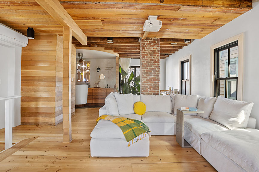 Cozy living room with white sectional, plaid throw, brick columns, and open kitchen.