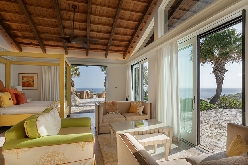 Airy living space with ocean view, green sofas, and yellow four-poster bed.
