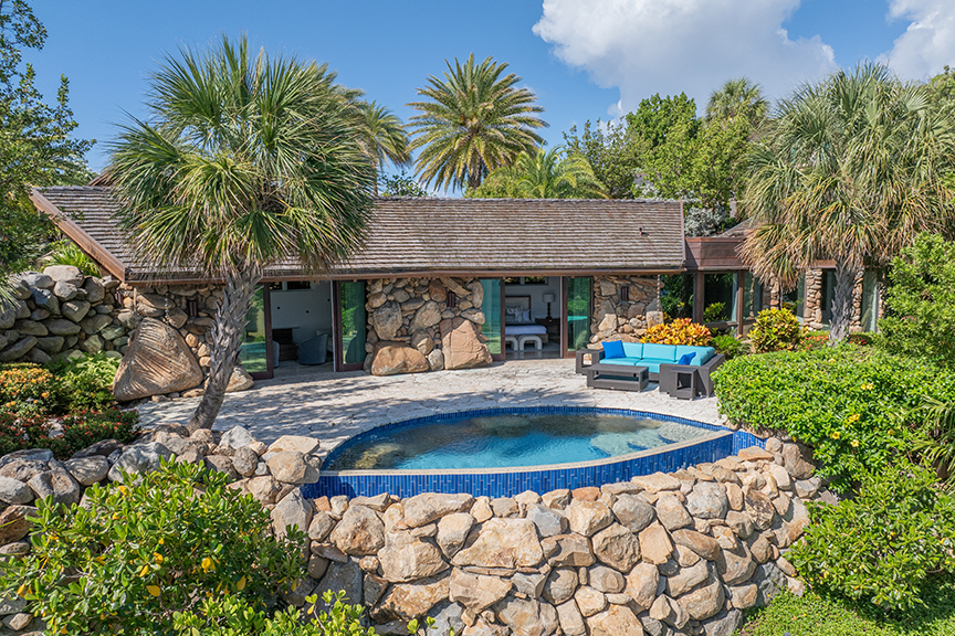 Stone house with thatched roof, pool, and palm trees.