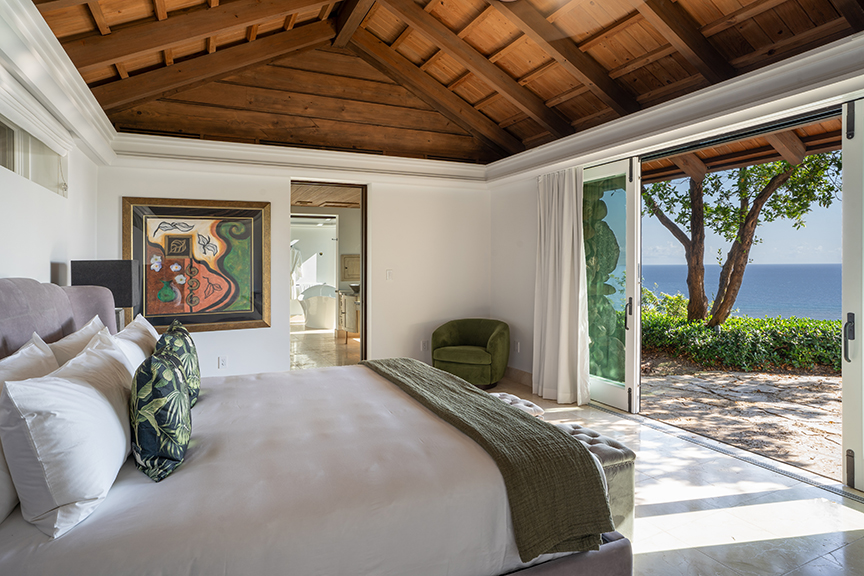 Bedroom with wooden ceiling, large bed, armchair, and ocean-view access.