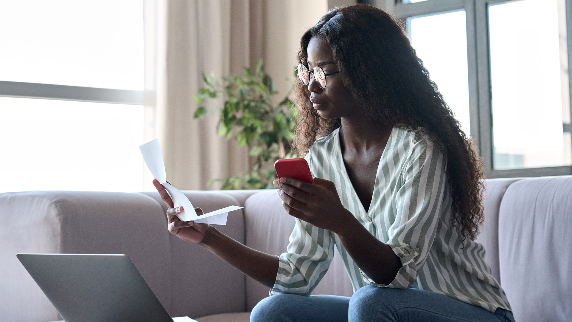 young black woman holding paper and paying bills with mobile phone
