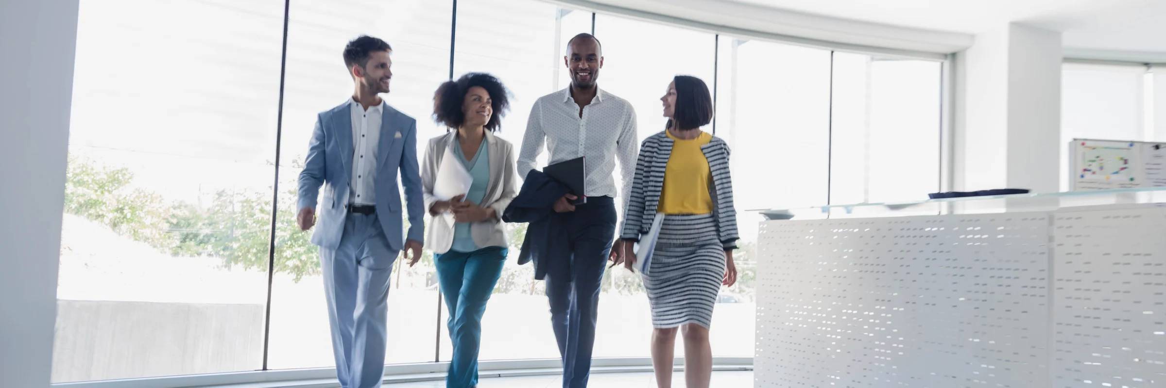 An image of four work colleagues of diversity walking together and smiling in an office