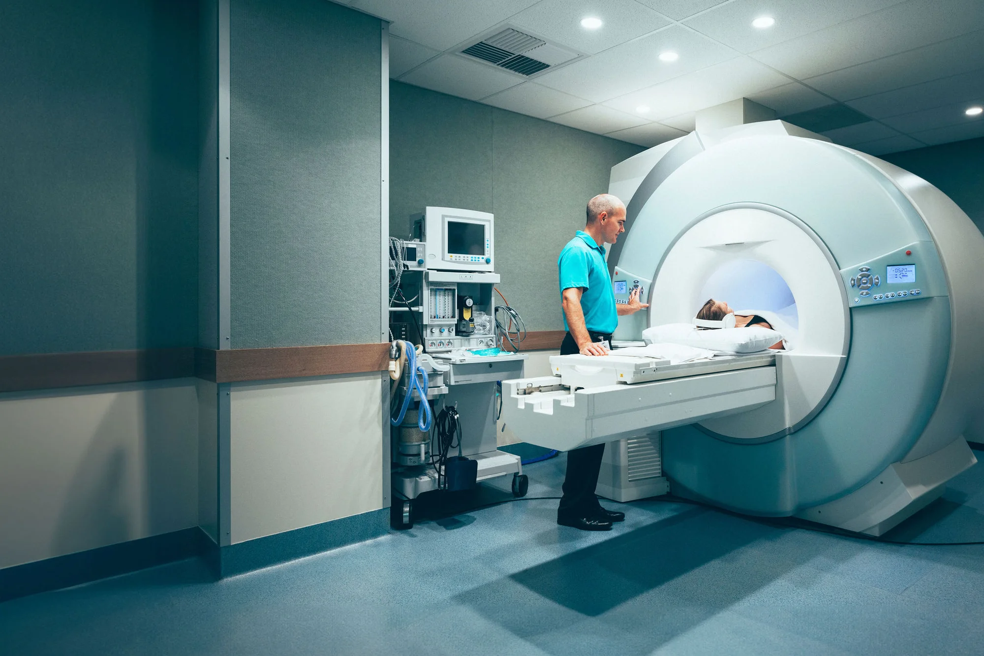 An image of a CT scan process taking place with a patient inside CT scanner while a technician administers the process