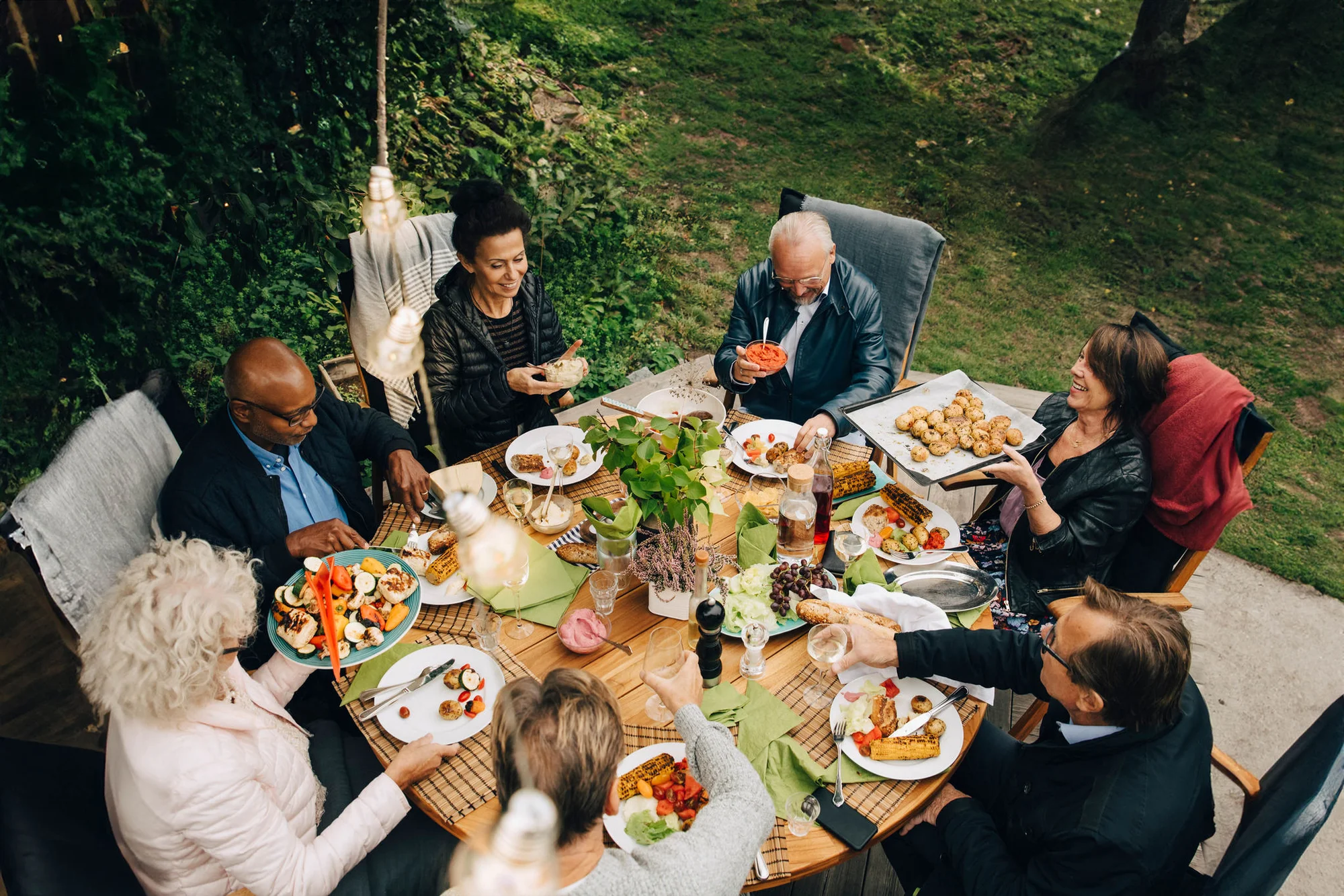 High angle view of senior male and female friends enjoying dinner at a dining table during a backyard garden party