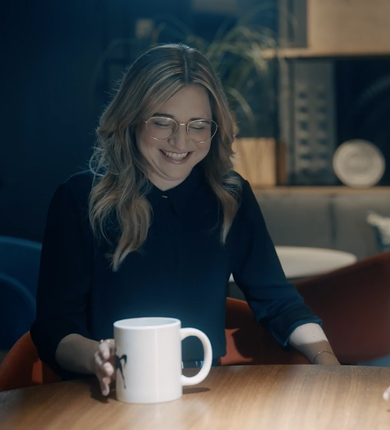 Lauren Schmeer smiling at a table with a cup of coffee in her hand