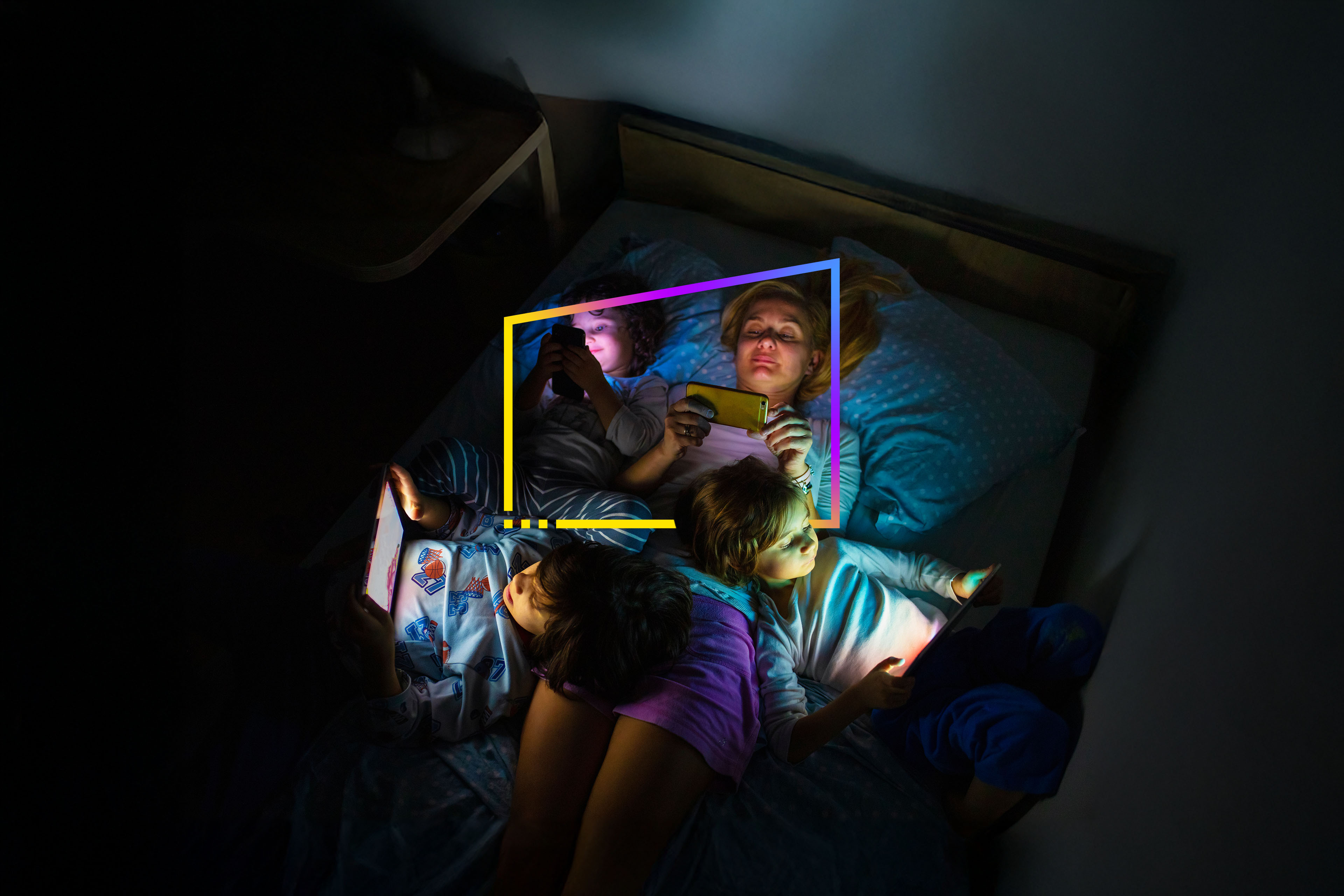 An image of a mother with her kids in bed looking a digital tablet in the dark