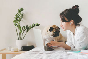 A woman and her pug dog working on the computer at home