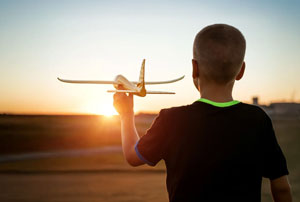 An image looking from the back of a young boy playing with a toy airplane during sunset