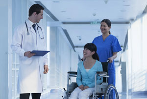 A nurse pushing patient in wheelchair talking to a doctor in a hospital hallway