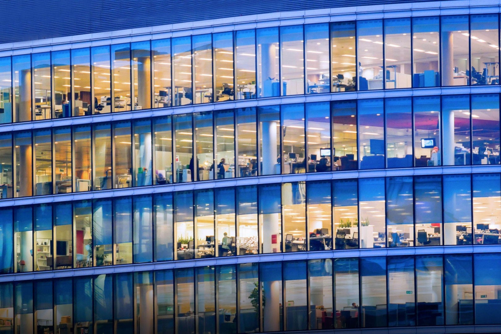 Image looking at a glass and steel office building showing multiple floors with office cubicles