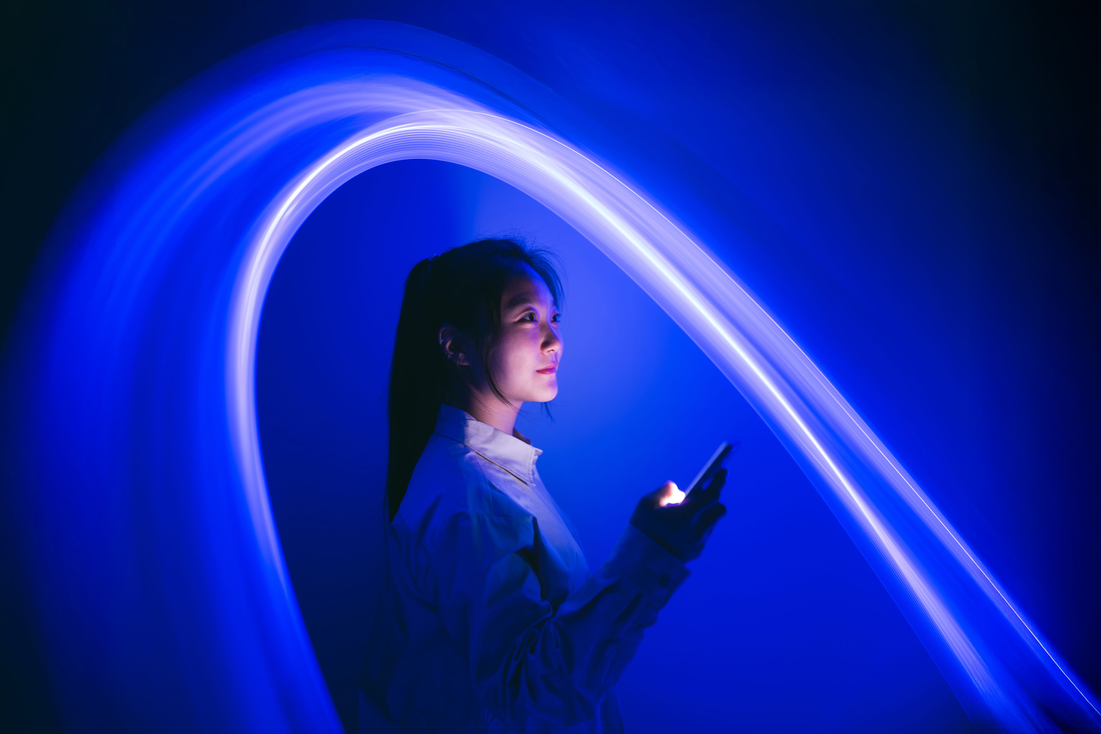 An image of a woman holding a smartphone with arc of light over her head