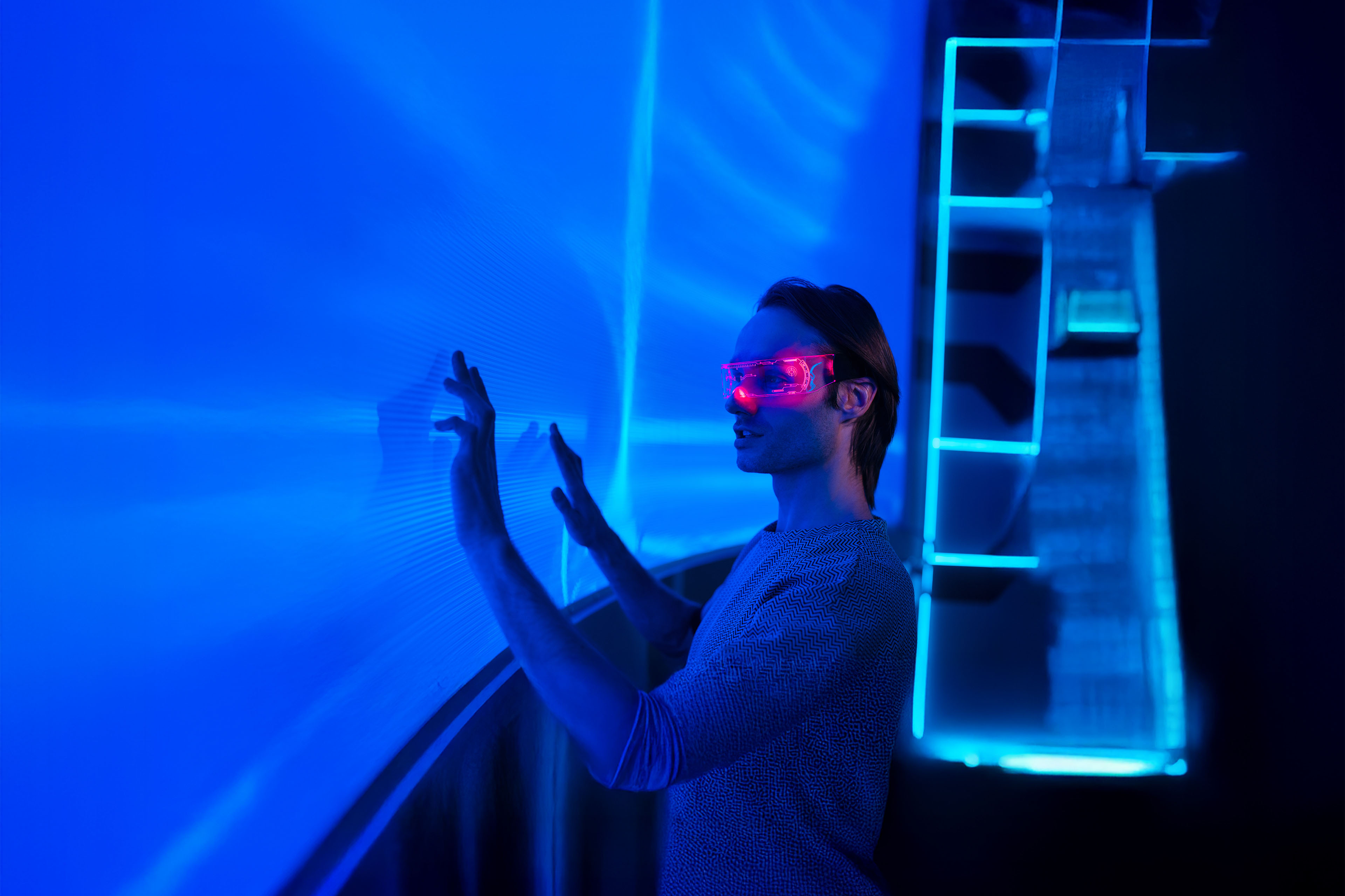 An image of a man wearing smart glasses interacting and placing his hands on an interactive digital screen