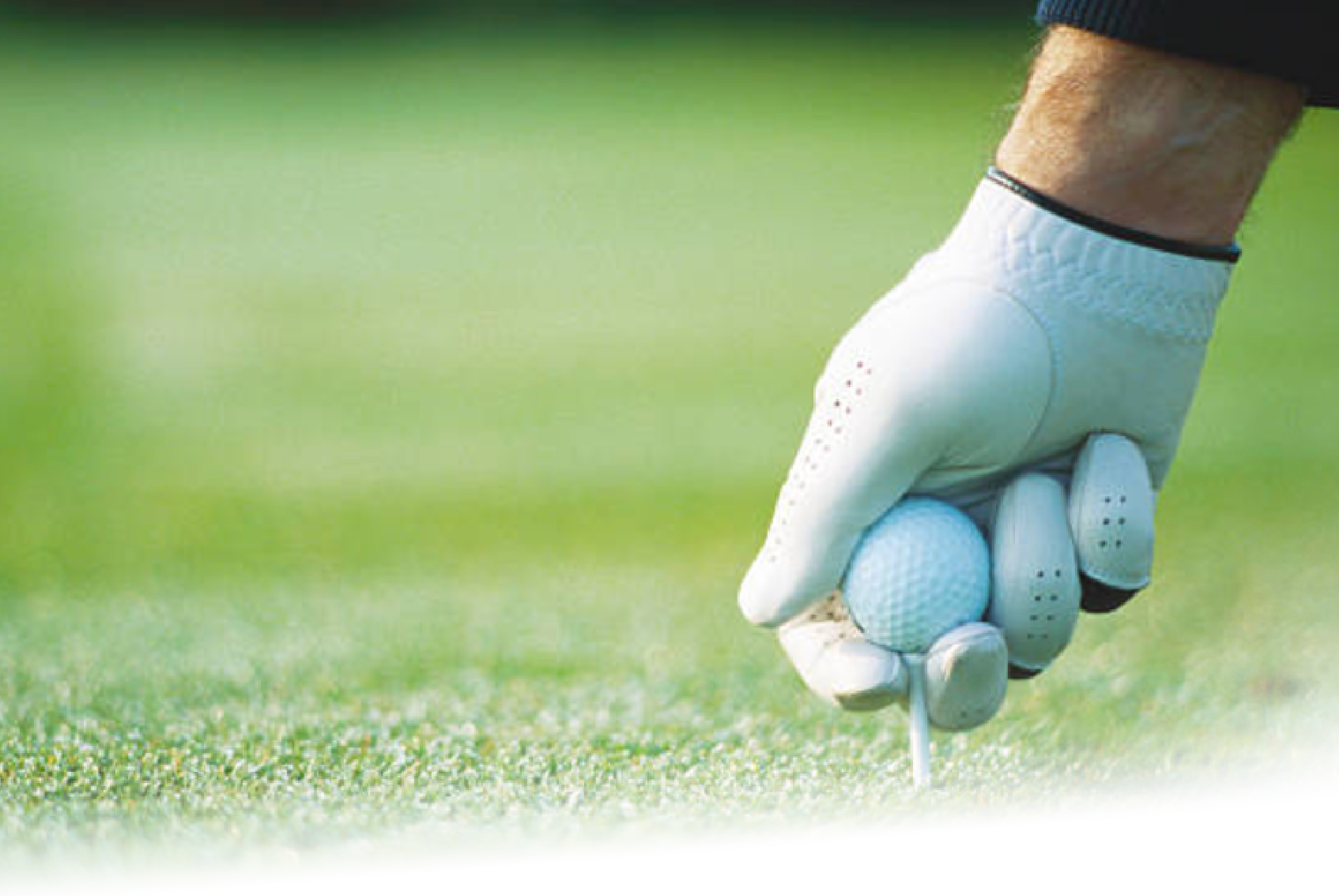 Close up shot of a white gloved golfer's hand around a golf ball and tee while placing it onto the green