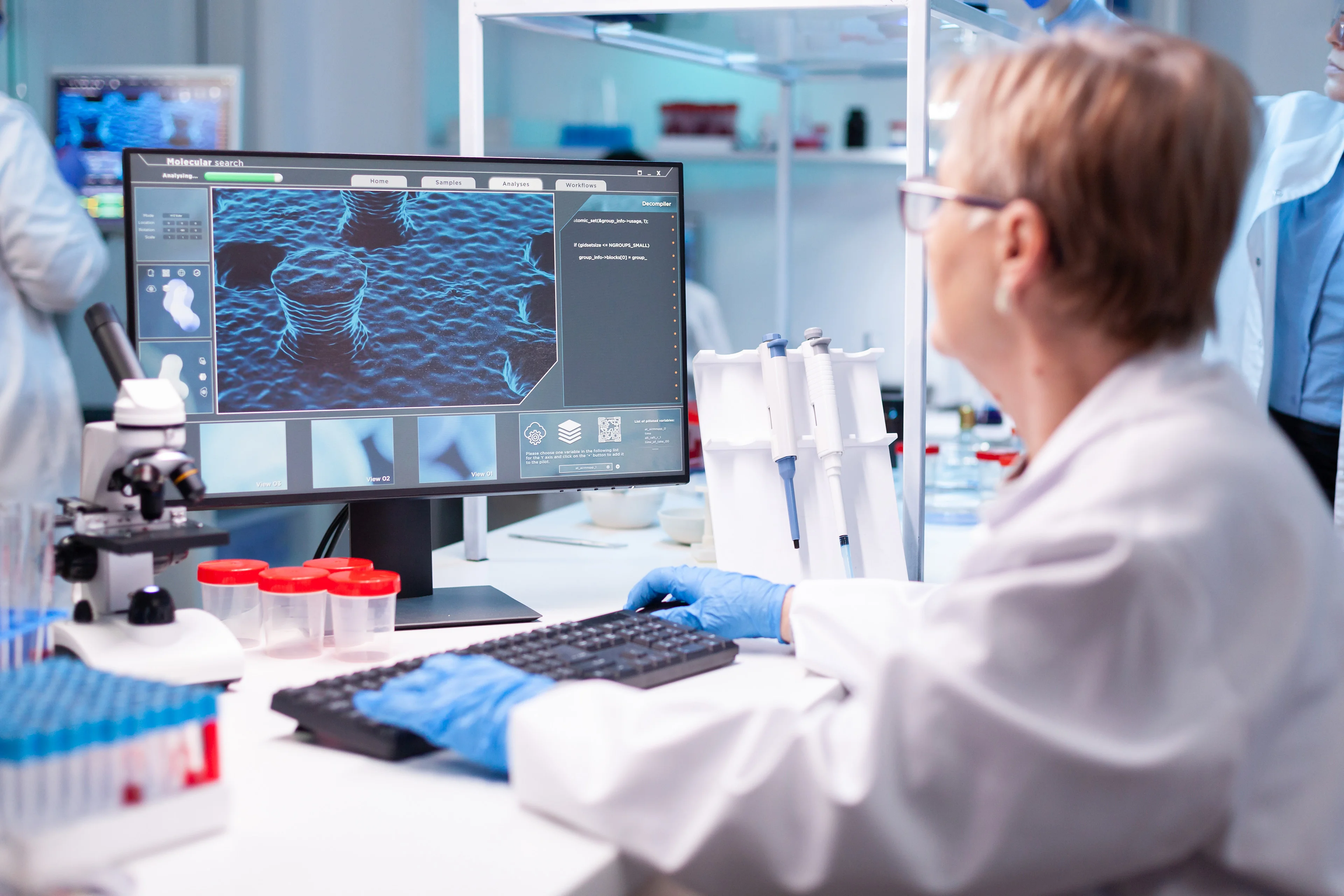 An image of a female doctor wearing gloves while analyzing a mold on a computer screen