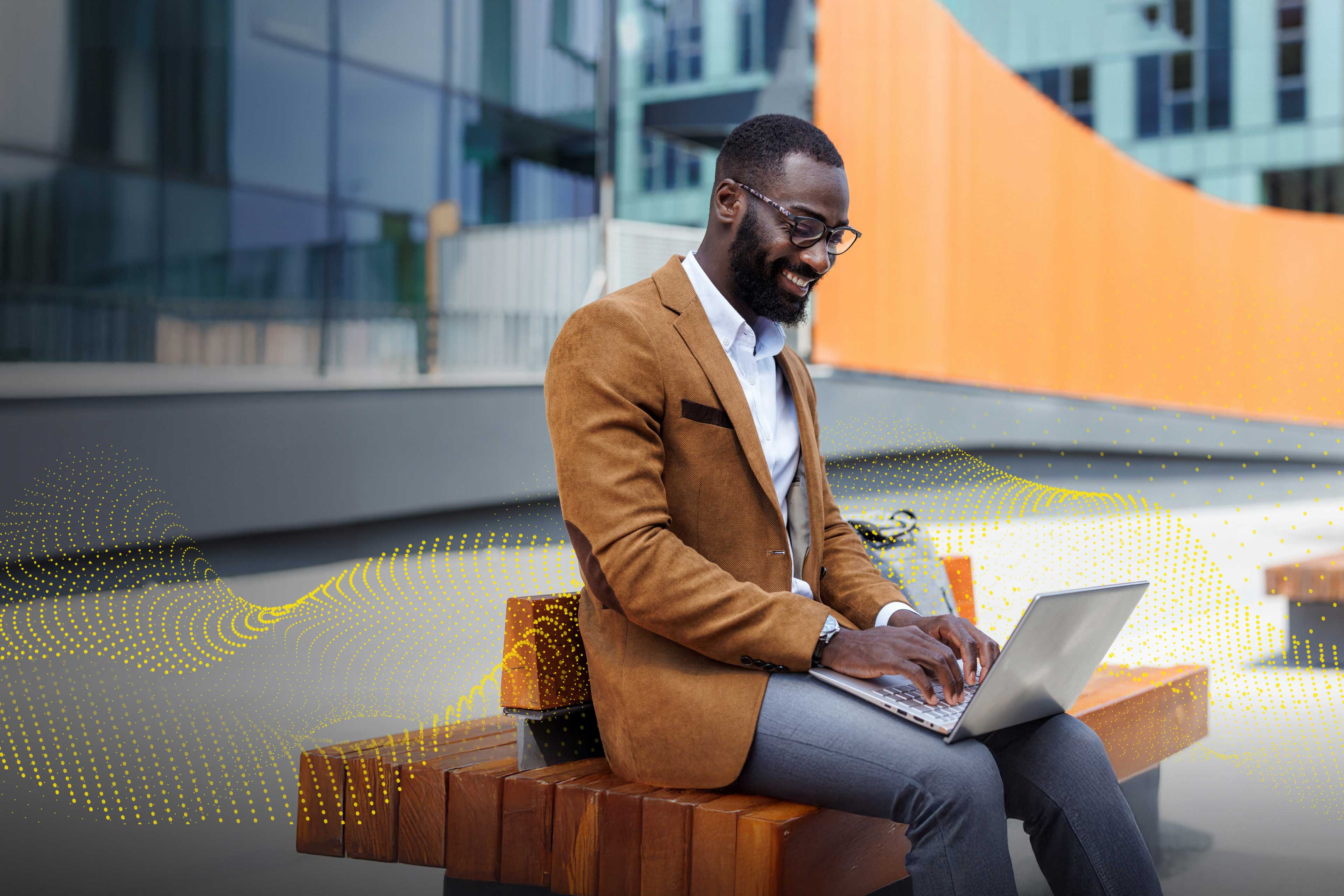 An image of a man in a suit sitting in an urban setting with his laptop.