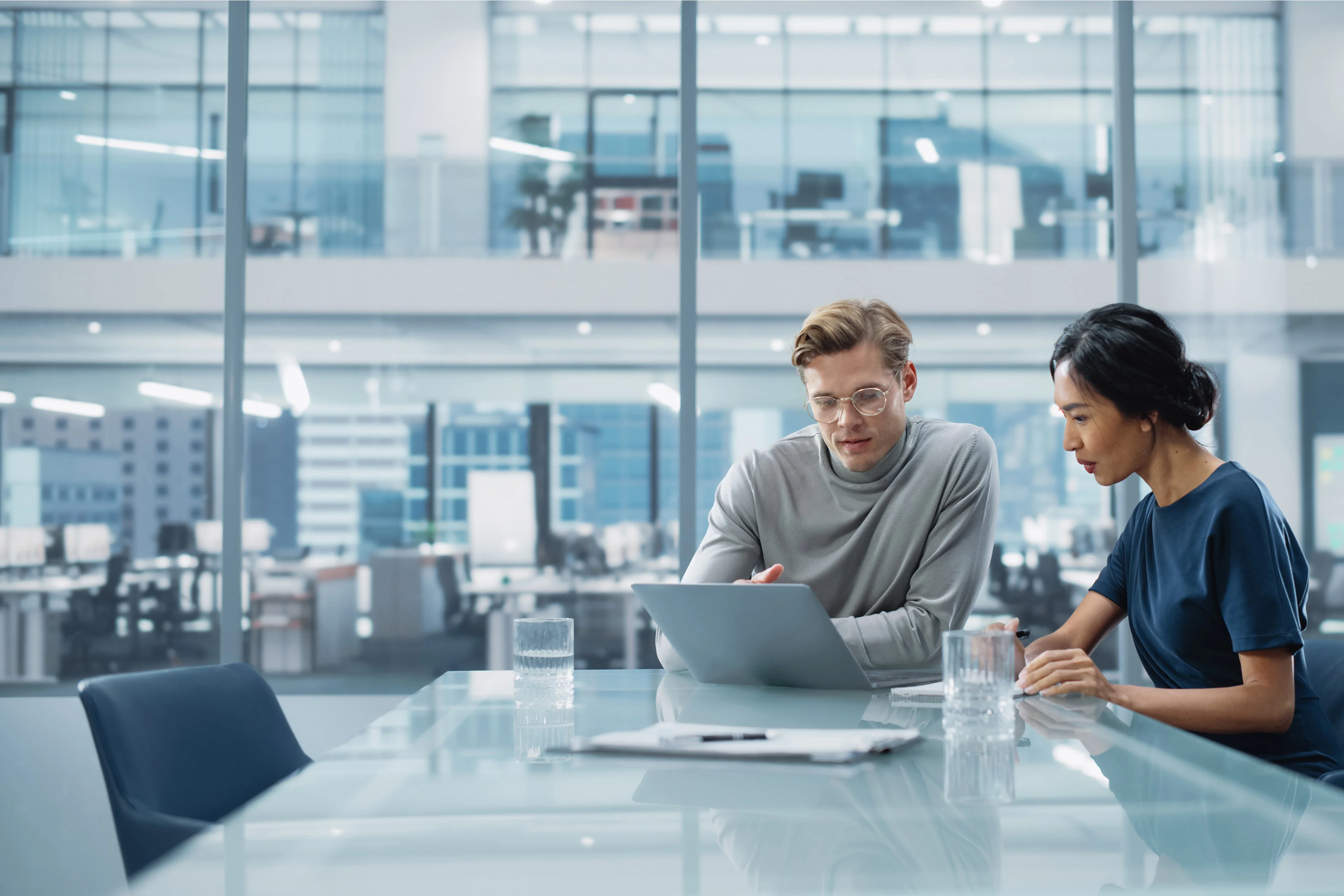 An image of two colleagues working together in a conference room in a modern workplace setting.