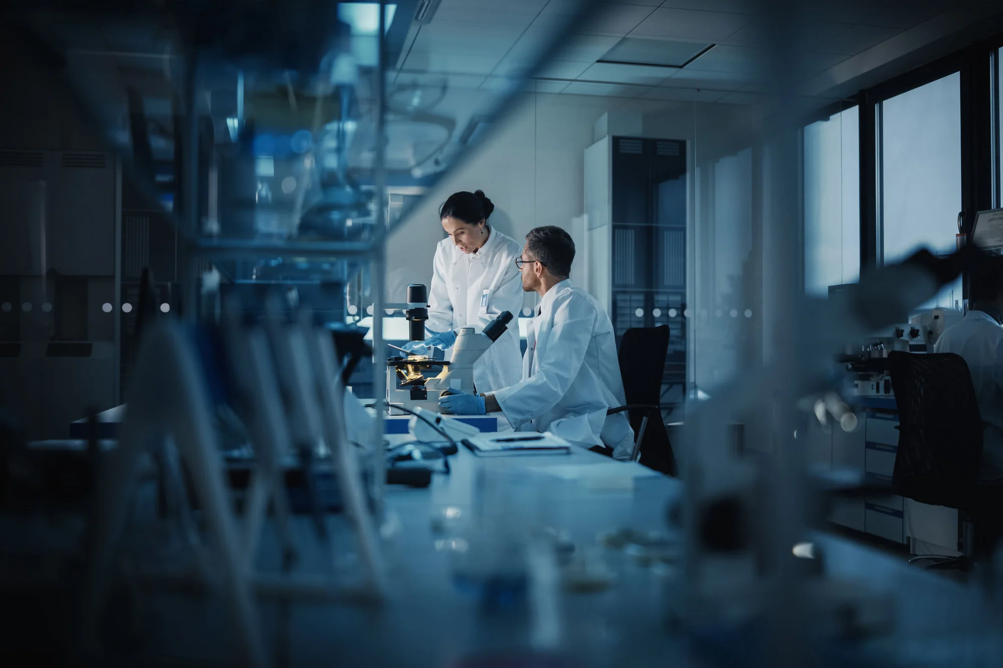 Image of two scientists in a lab reviewing samples at a microscope