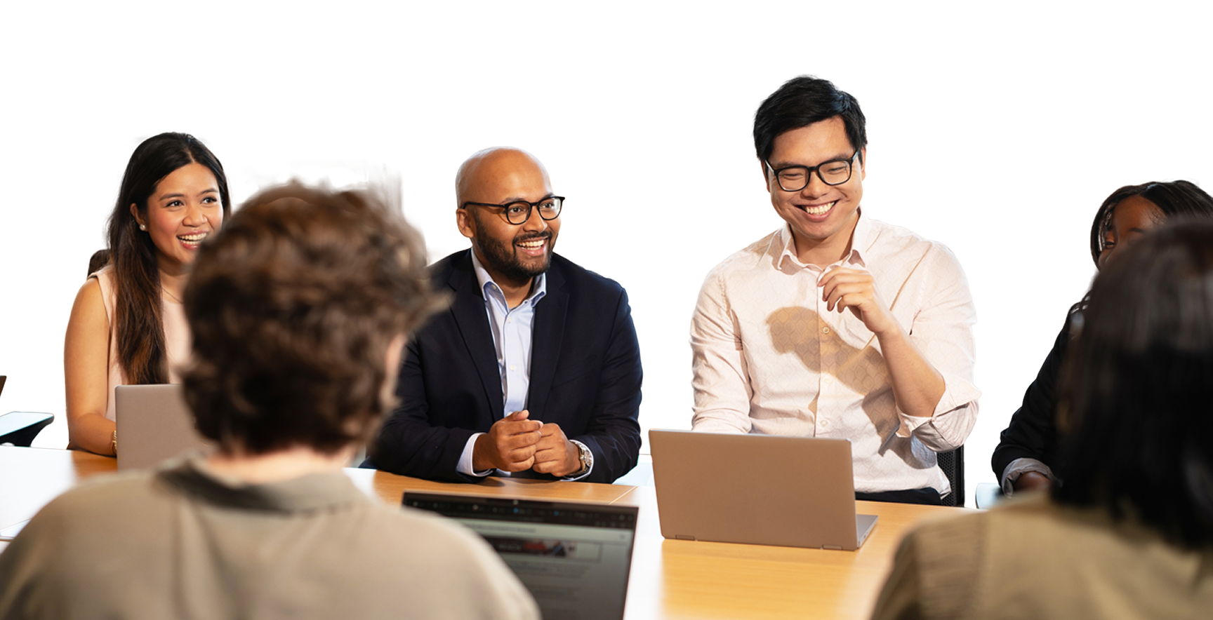 team of people gathering around a conference table with their laptops smiling at one another and collaborating