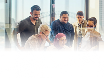 team of people inside an office huddled over a colleague's desk looking over work