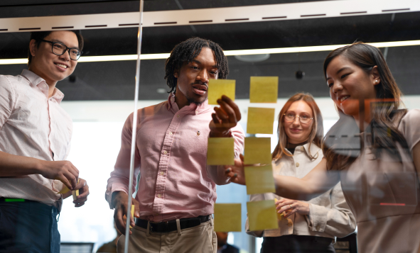 group of professionals brainstorming and placing ideas on post-it notes and applying to glass wall